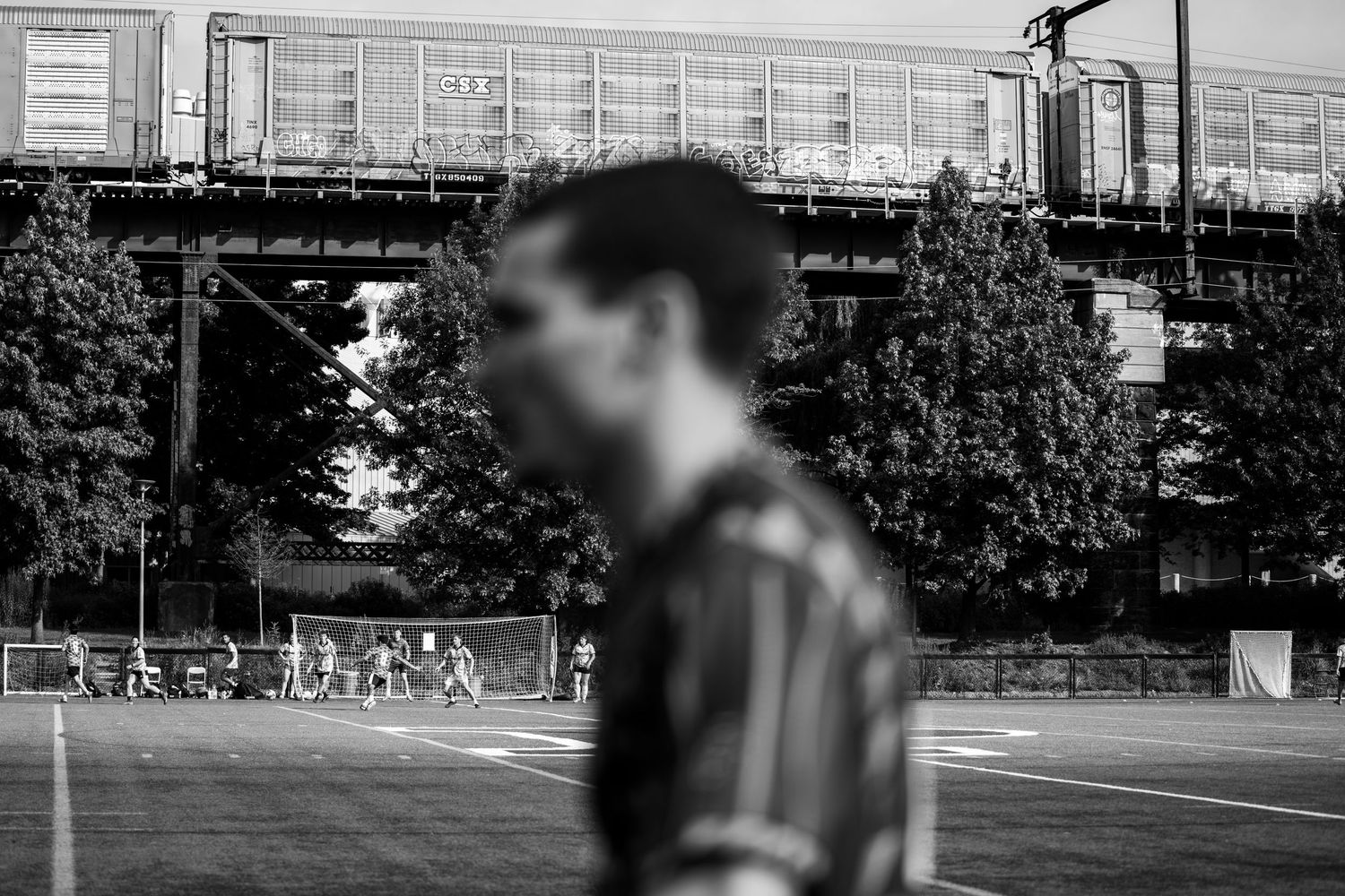 Black and white photo of a man standing near a sports field with an elevated structure behind.