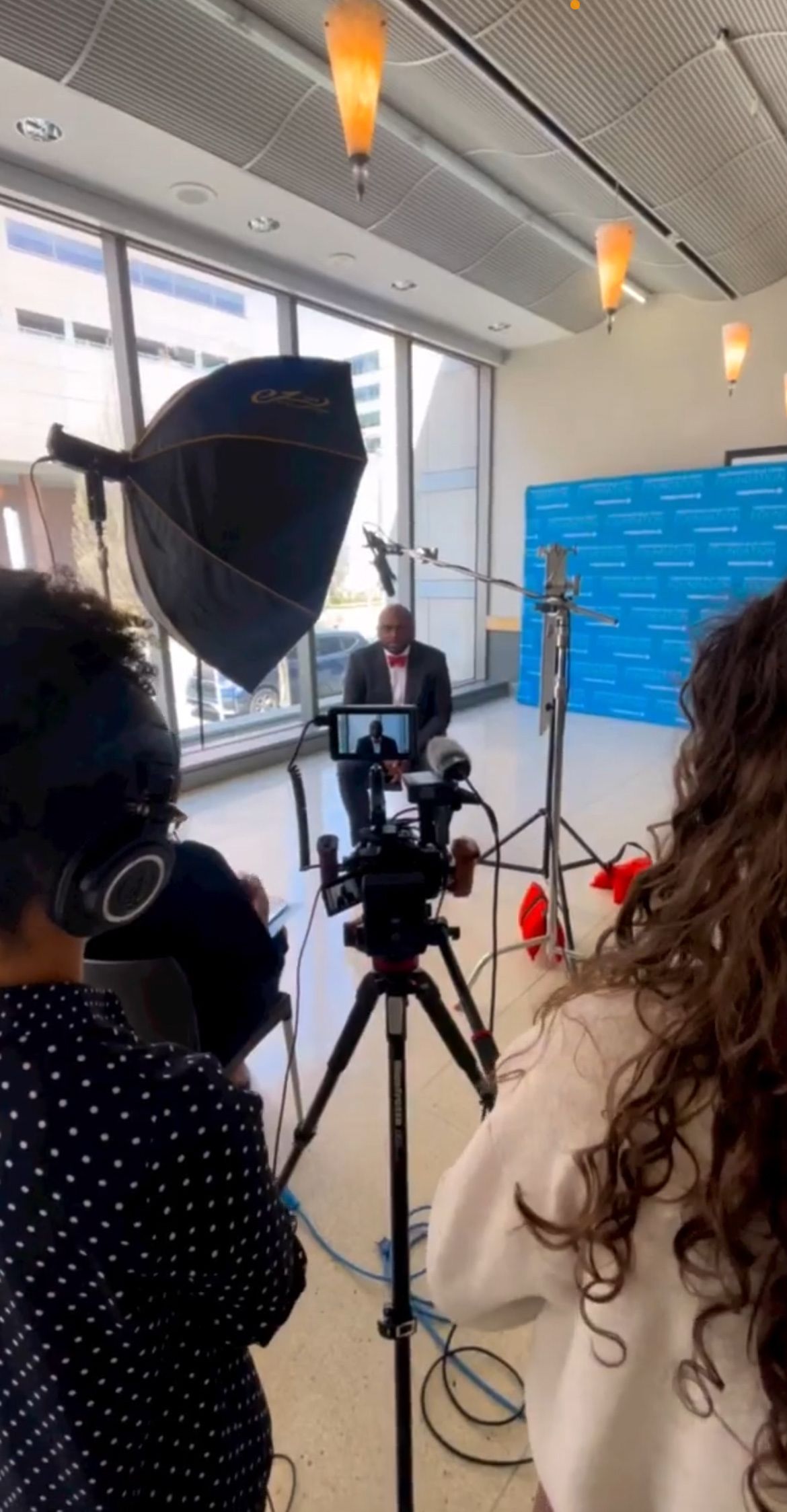 Professional video interview setup with camera, lighting equipment, and subject before a blue backdrop.