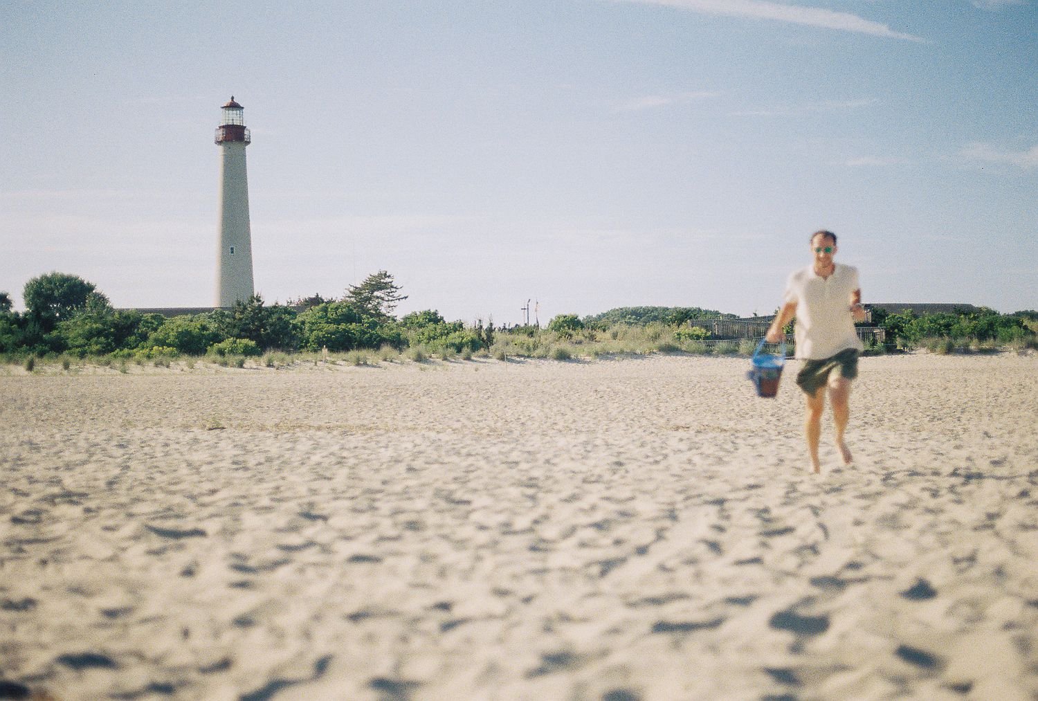 Man running on sandy beach with historic Cape May lighthouse standing tall in background.