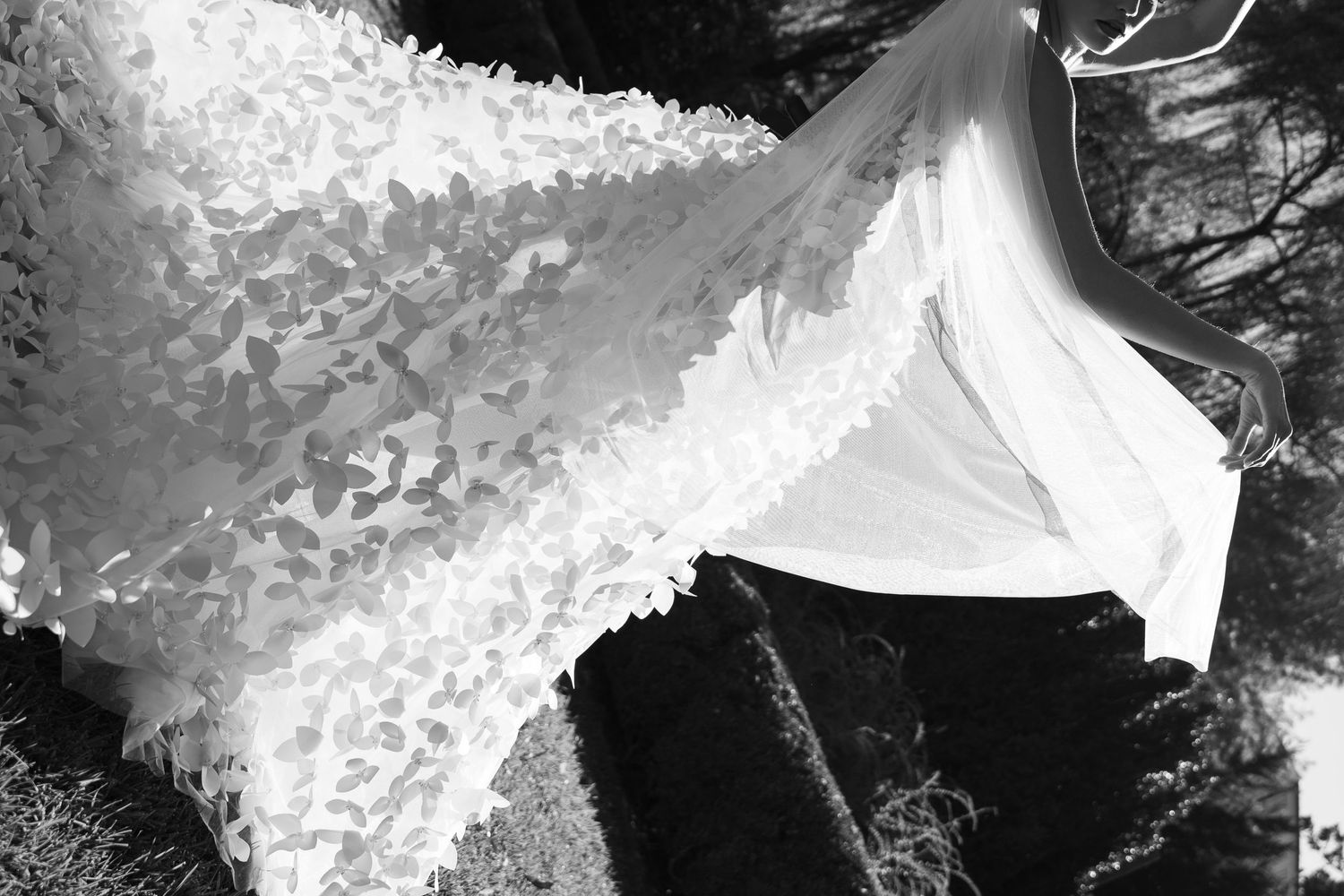 Black and white close-up of an intricate lace wedding veil with floral appliques draped over a dark surface.