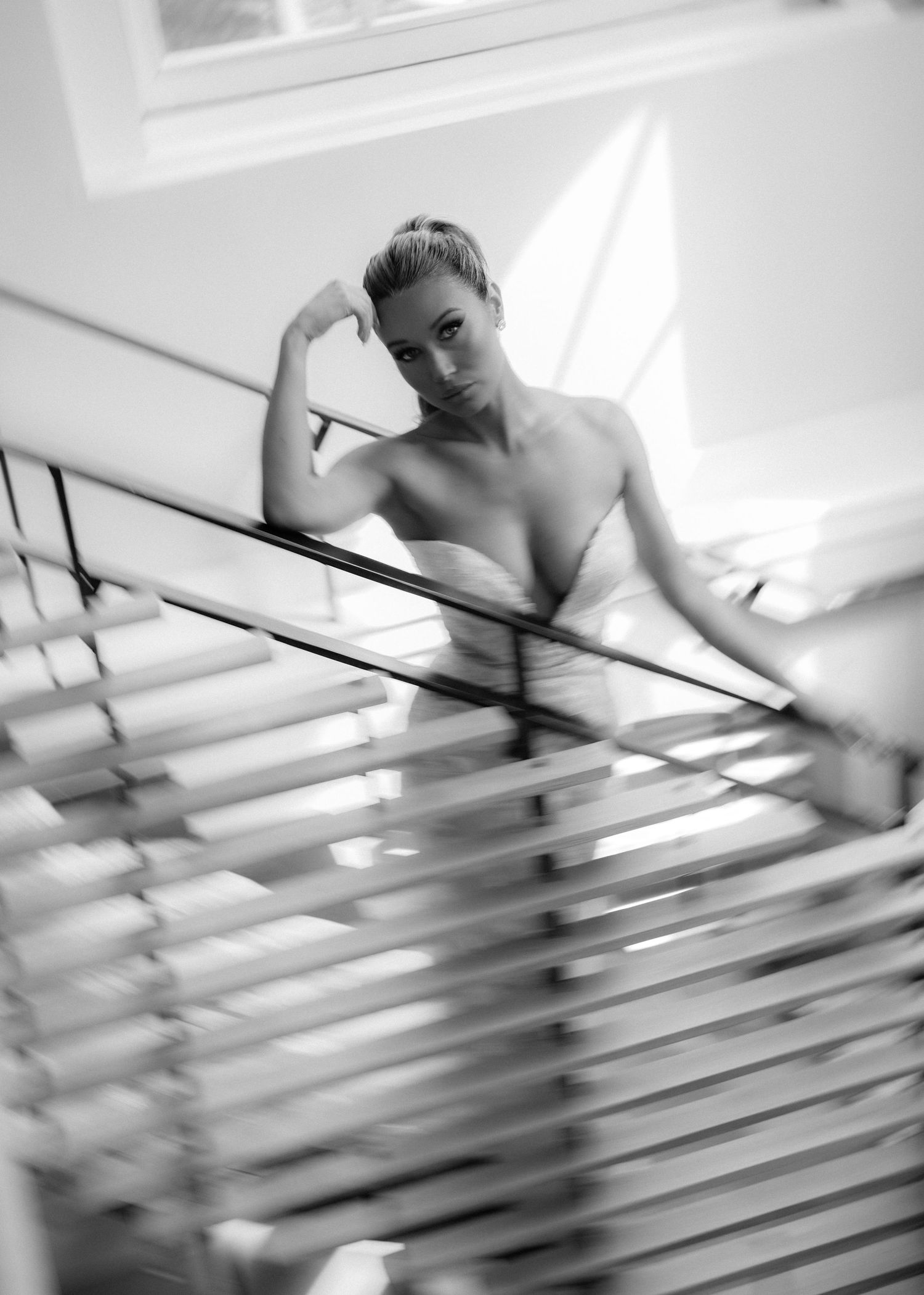 Black and white photo of elegant bride in strapless gown posing on modern staircase with railings.