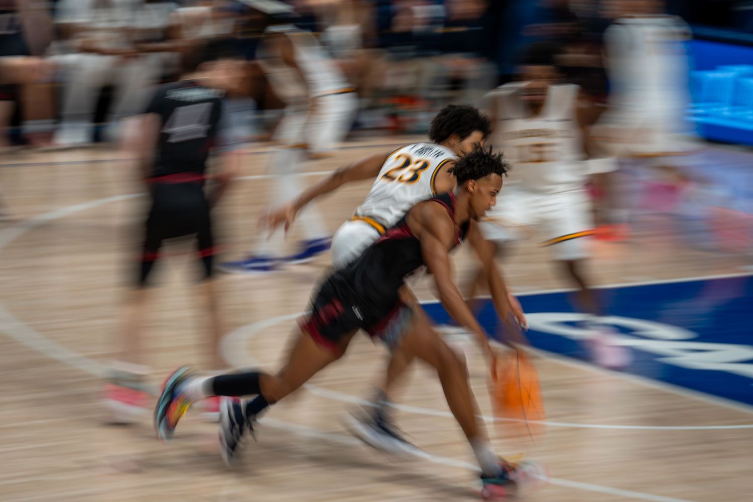 Motion blur action shot of two college basketball players competing for ball possession during game.