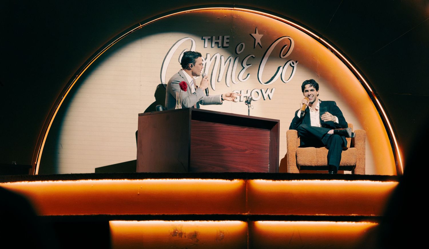 Two performers on stage under a vintage-style sign reading The Connie Co Show with warm lighting.