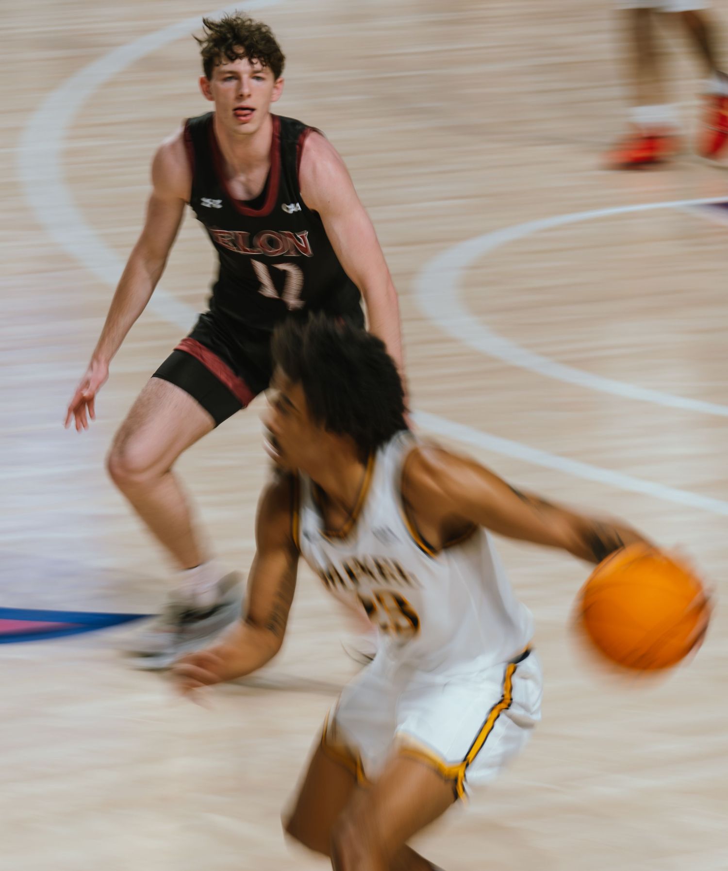 Motion blur photo of college basketball player dribbling past Elon University defender number 17.