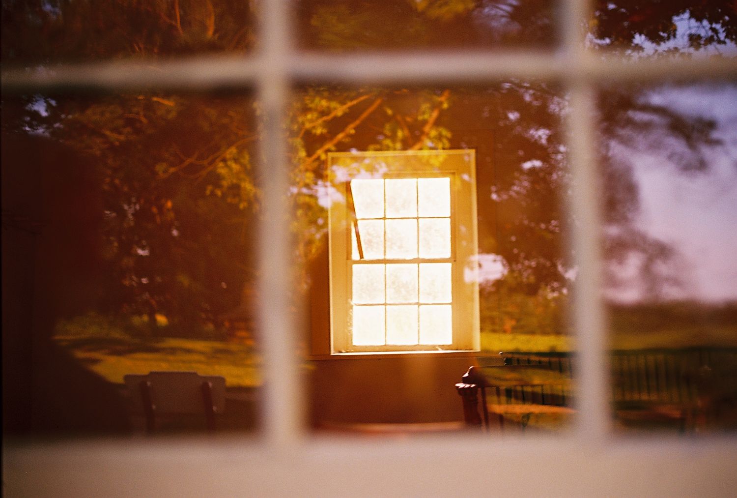 View through a window pane of a glowing white window on a sunlit building surrounded by autumn trees.