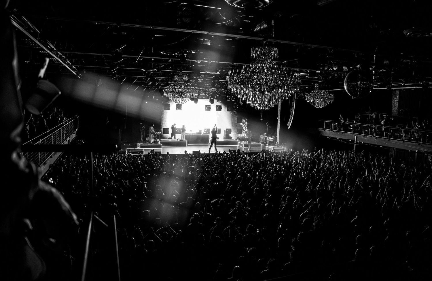 Black and white wide-angle shot of concert venue with crowd and bright stage lights.