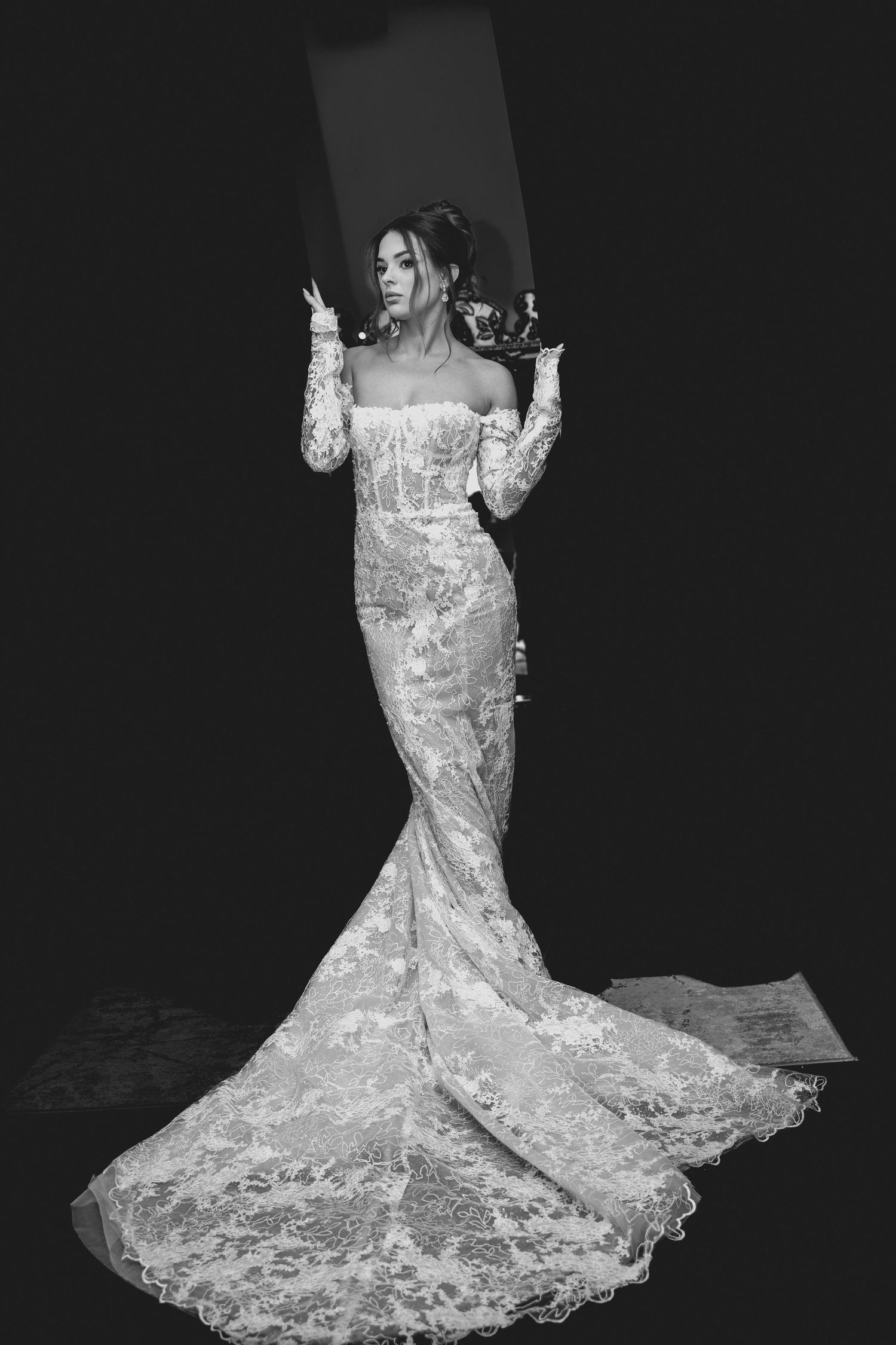 Stunning bride in fitted lace mermaid wedding gown with long train posing dramatically in black and white.