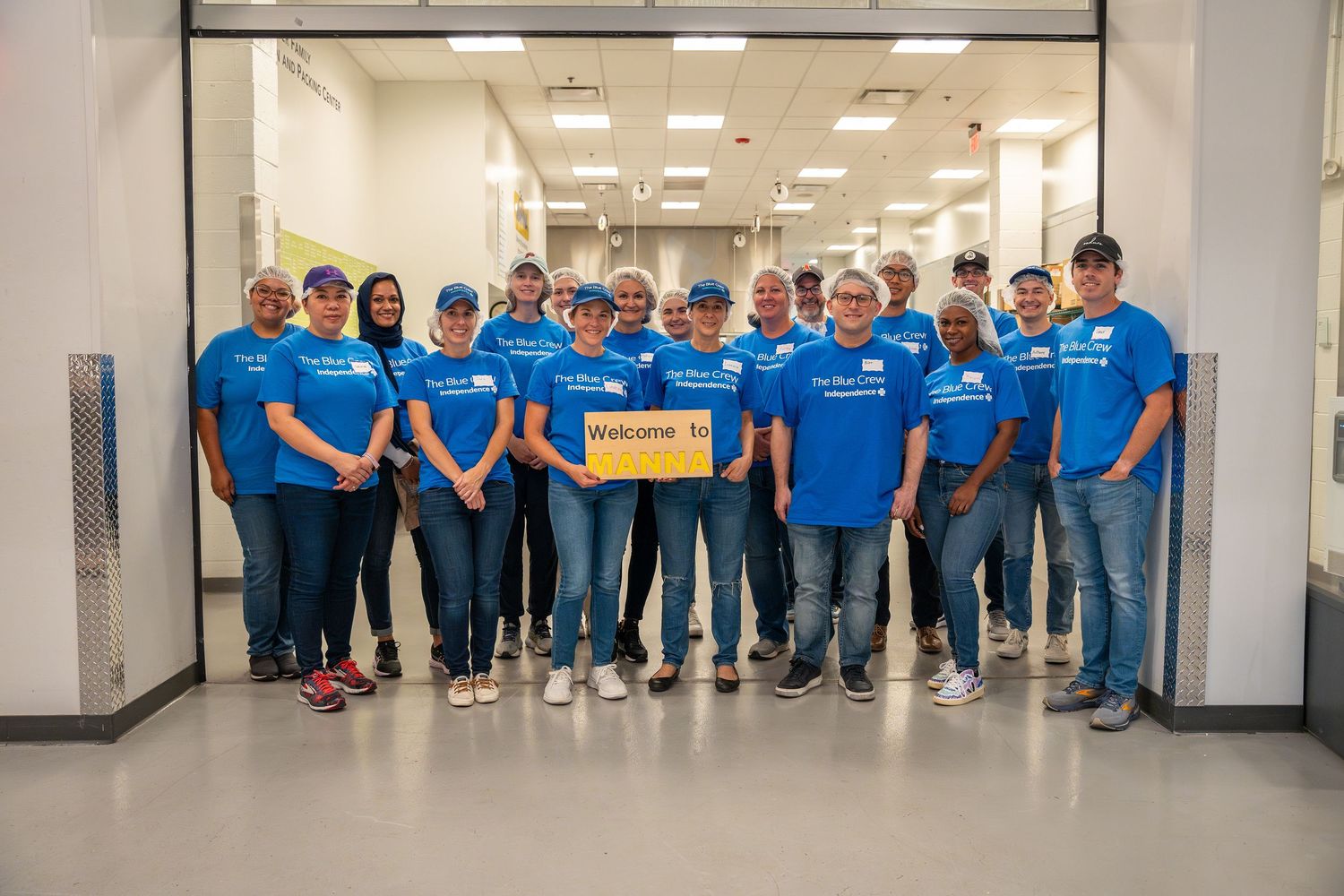 A large group of volunteers in matching blue IBX shirts pose together smiling inside a building.