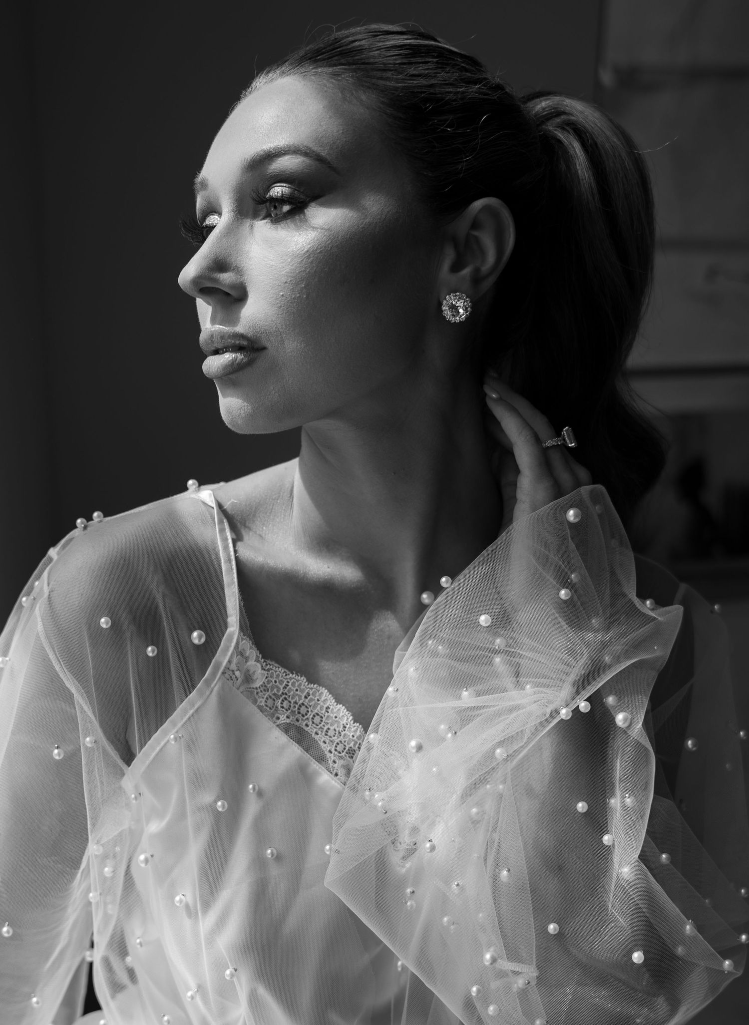 Black and white portrait of elegant woman in pearl-embellished sheer white gown with ponytail.