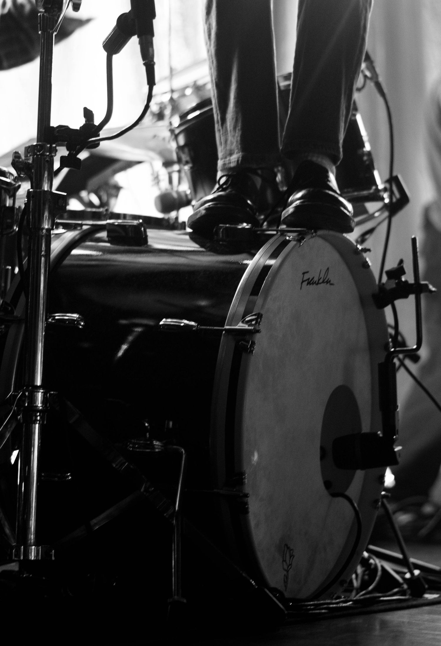 Black and white close-up of a bass drum with a performers feet standing on it during a live show.