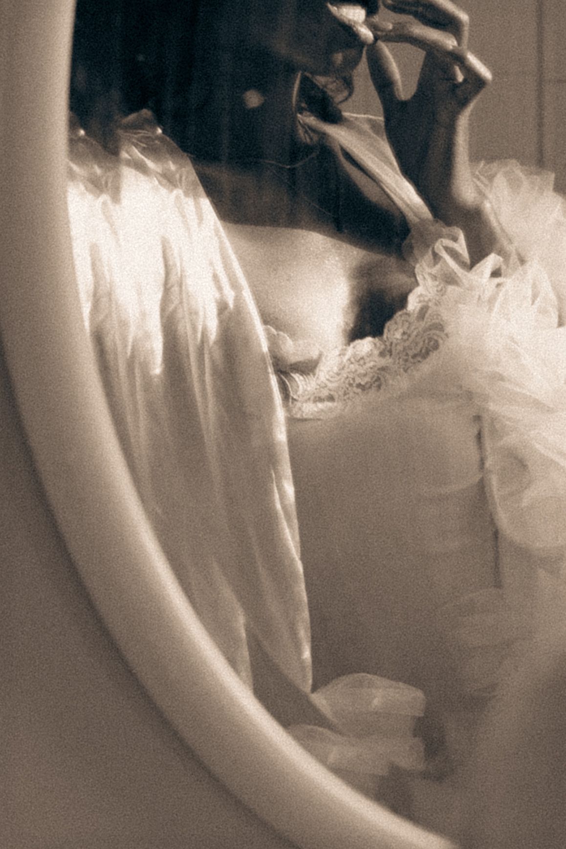 Dreamy sepia-toned mirror reflection of a bride in a lace wedding dress adjusting her veil.