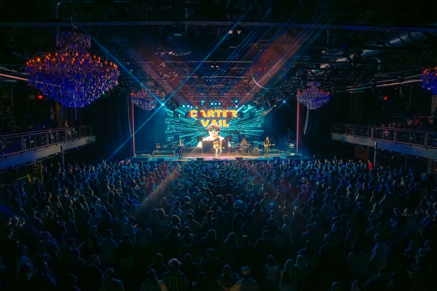 Packed concert venue with crowd and colorful stage lighting at Carter Vail performance.