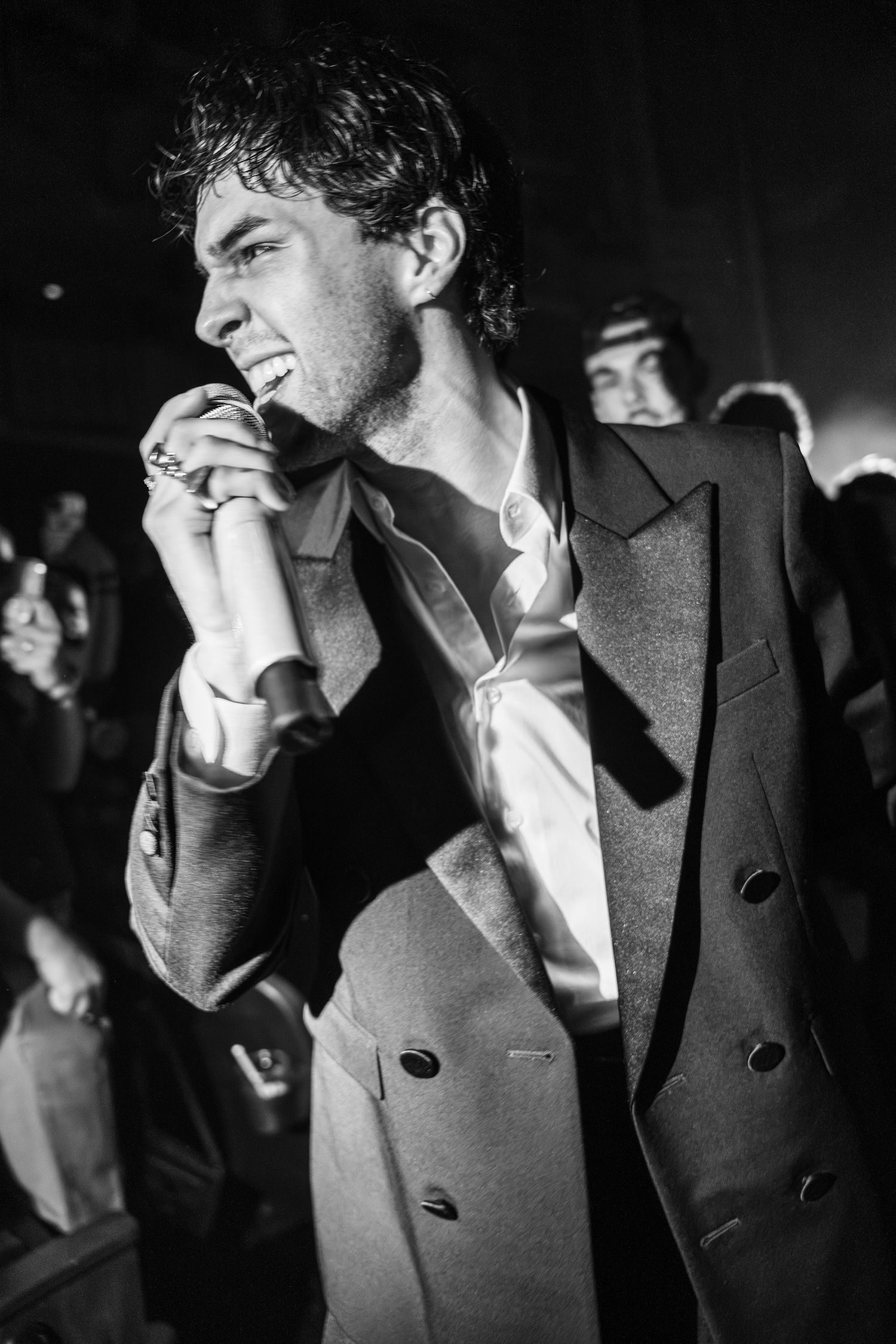 Black and white photo of a young man in a double-breasted suit holding a microphone at a concert.