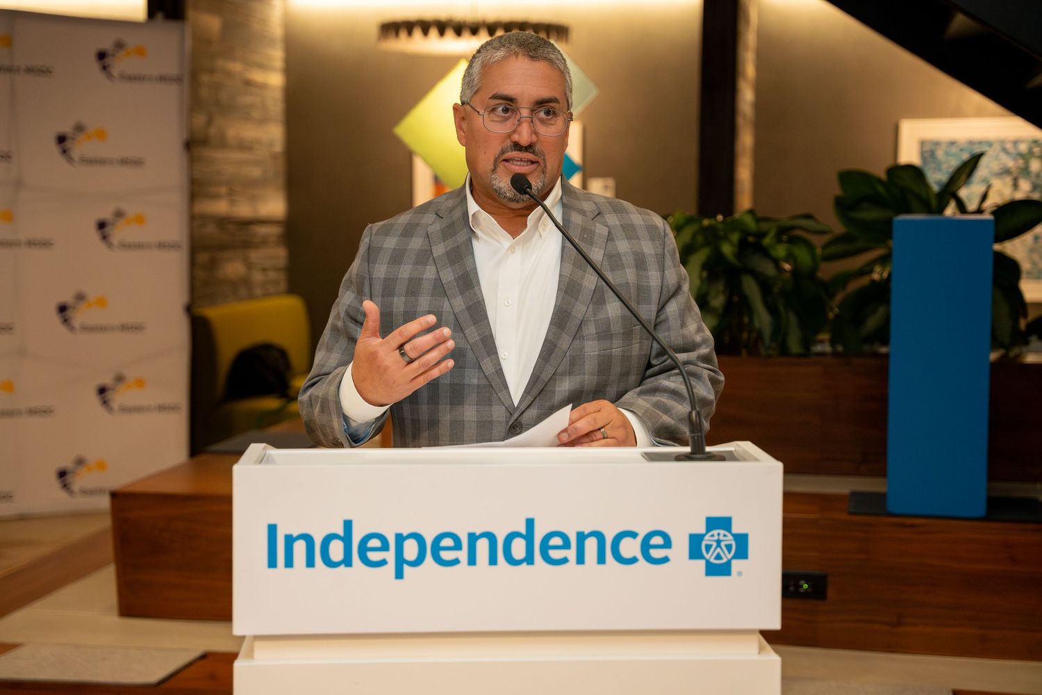 A man in a plaid blazer speaking at an Independence Blue Cross podium.