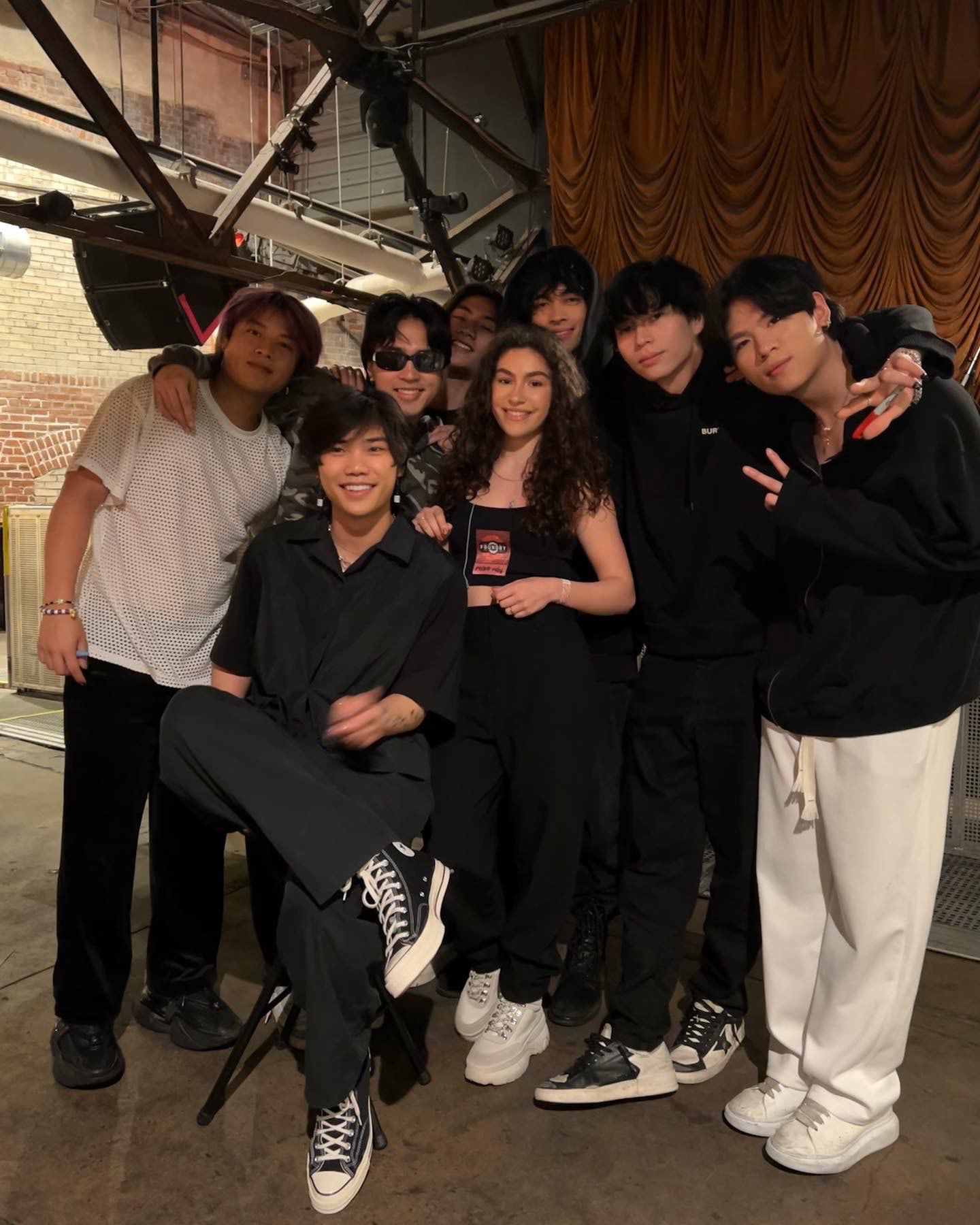 Group of young people posing together and smiling at an indoor venue with stage lighting above.