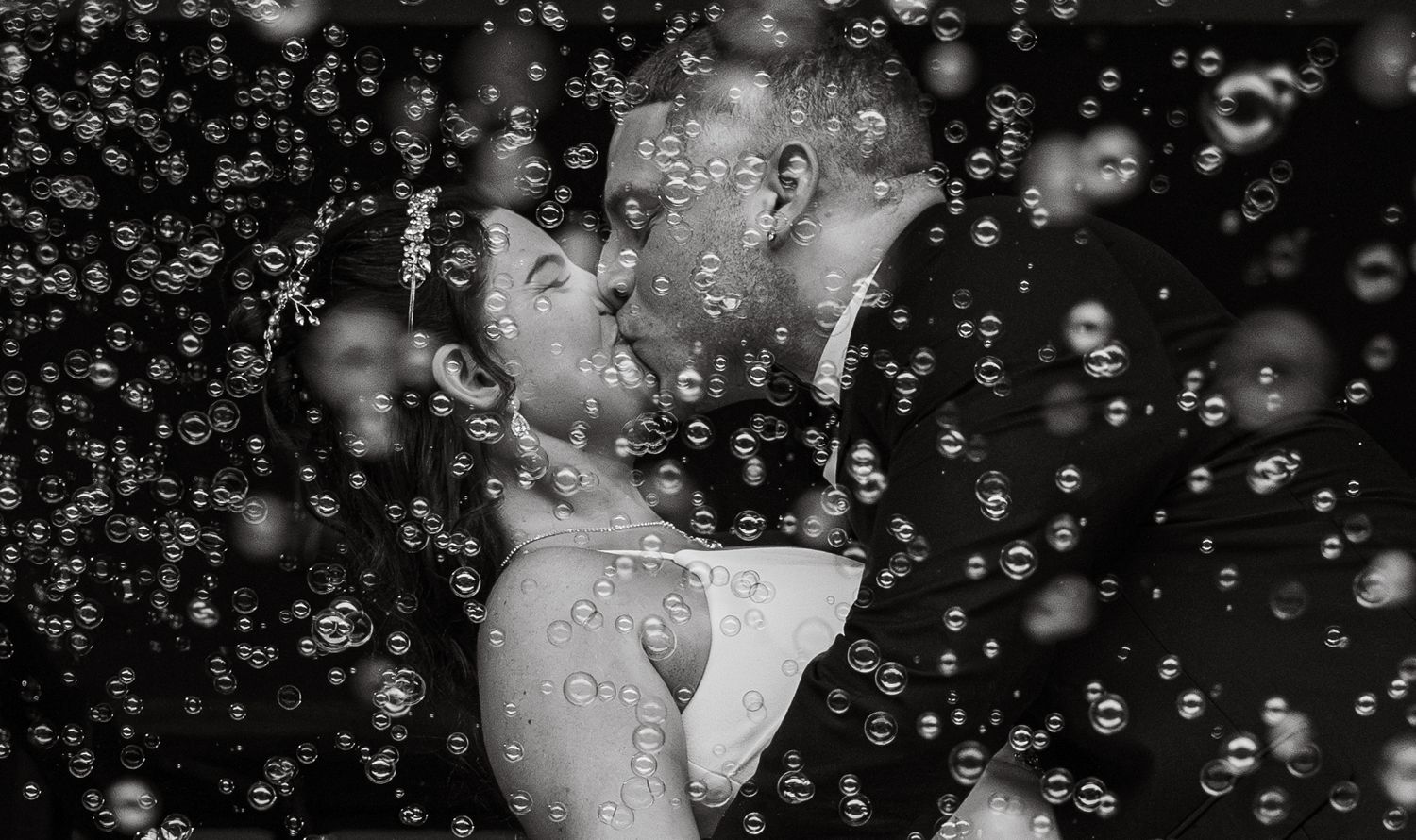 Romantic black and white photo of bride and groom kissing through bubbles.