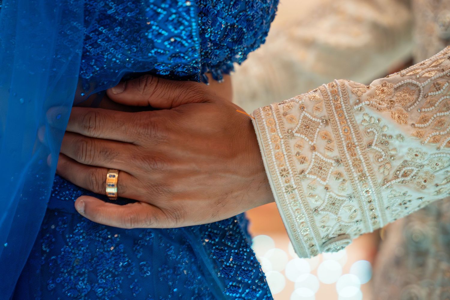 Groom's hand with gold wedding band resting on bride's blue lace wedding dress.