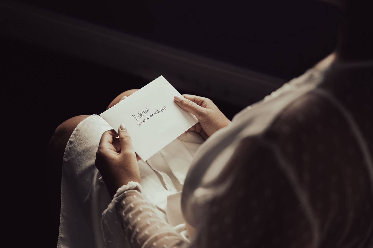 Bride reading a heartfelt wedding letter in soft light from above.