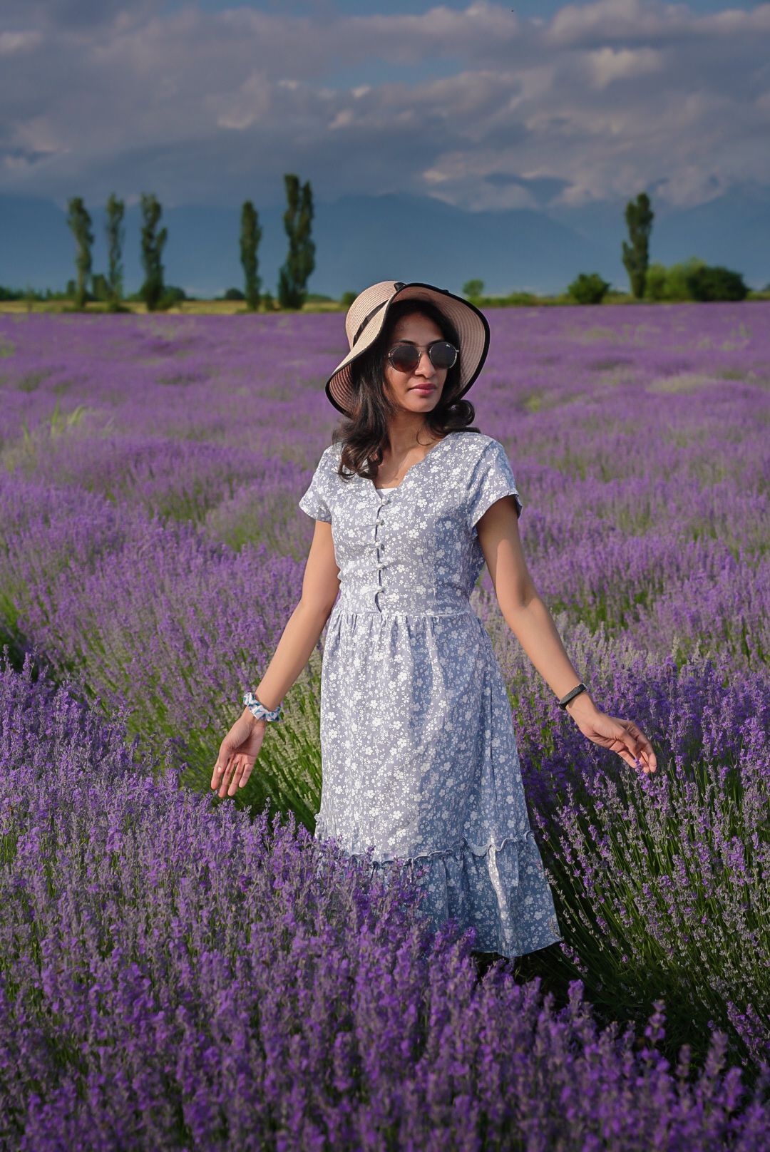 Woman in floral dress walks through blooming purple lavender field on sunny day.