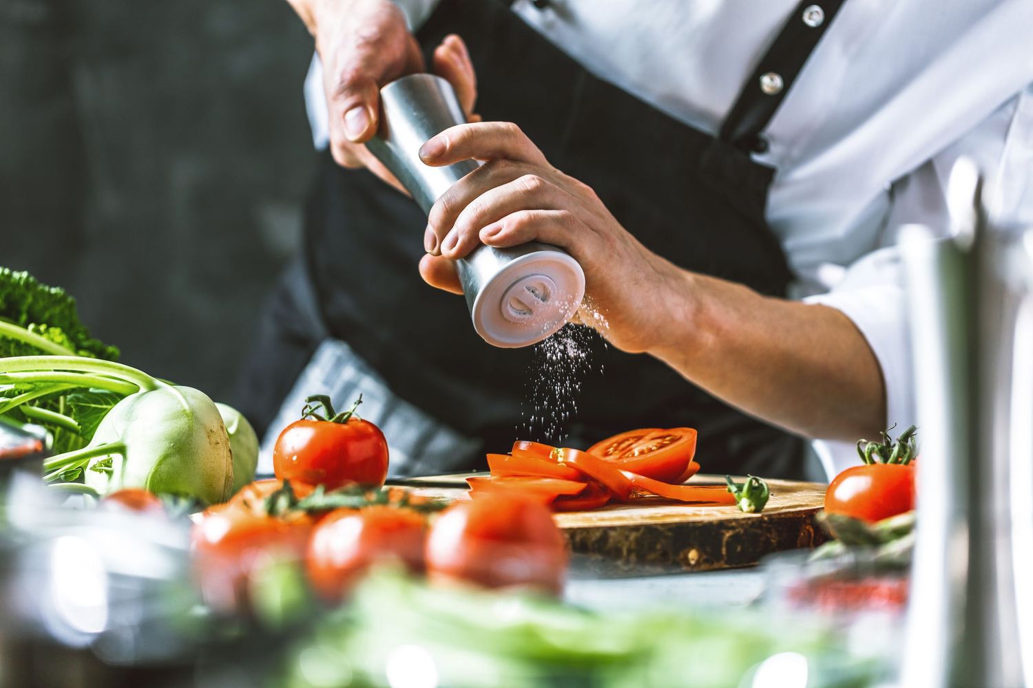 Chef chopping fresh vegetables on wooden cutting board in professional kitchen.