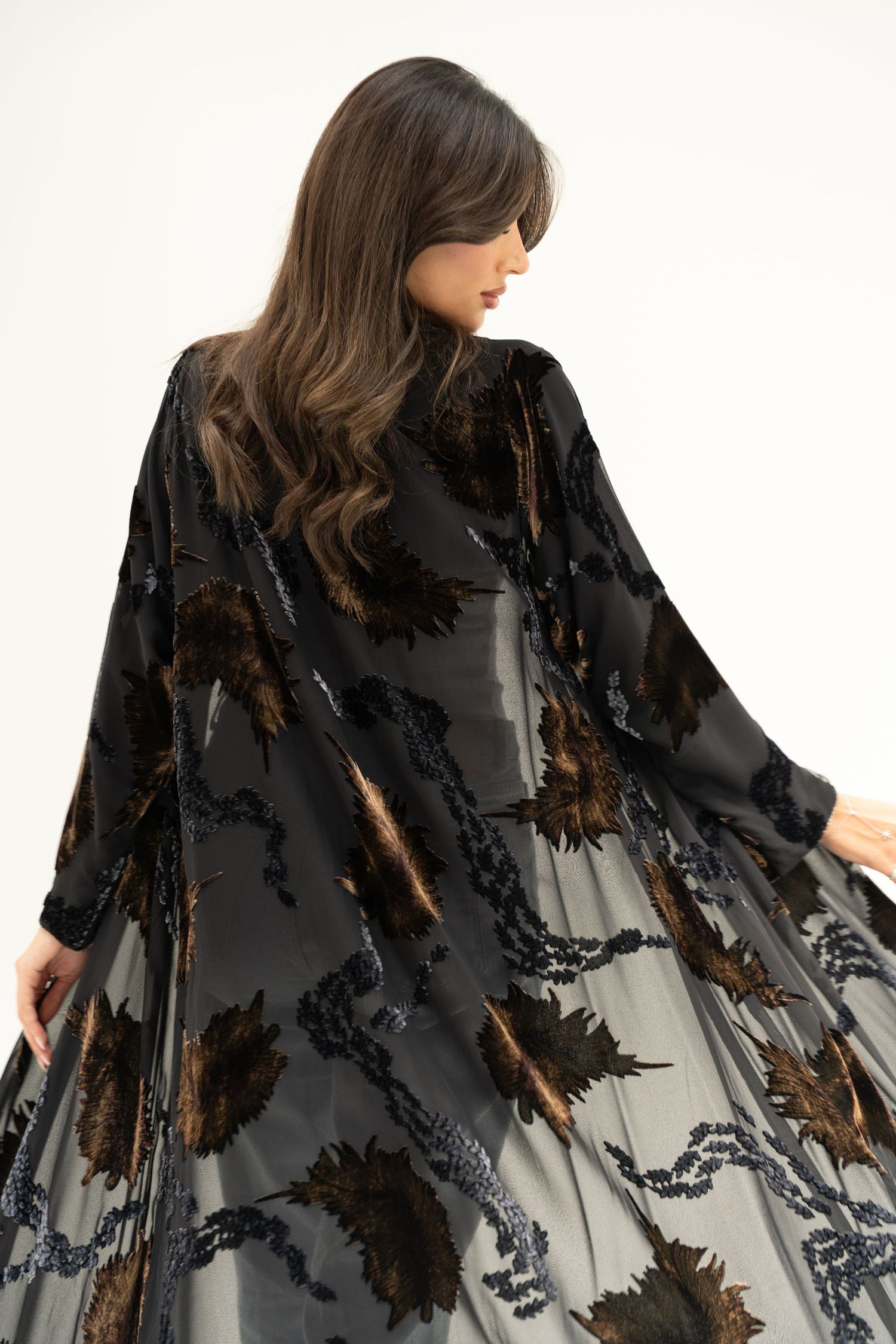 Fashion model wearing black sequined kimono robe with dramatic flowing sleeves against white background.