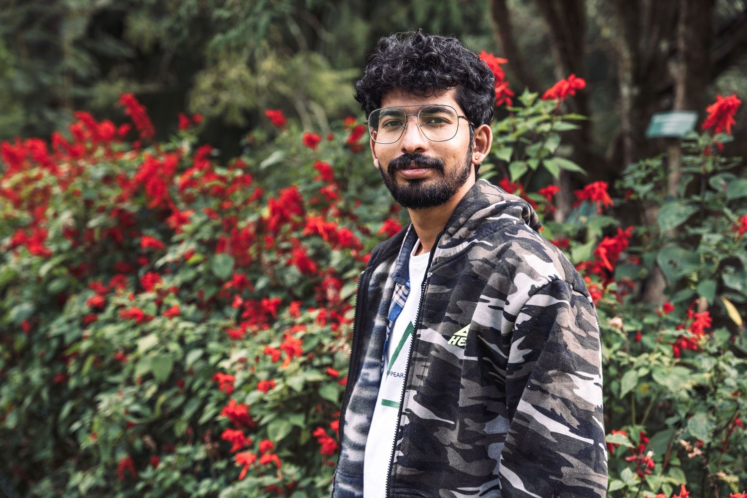 Portrait series in a garden with red flowers and a casual outfit against natural greenery.