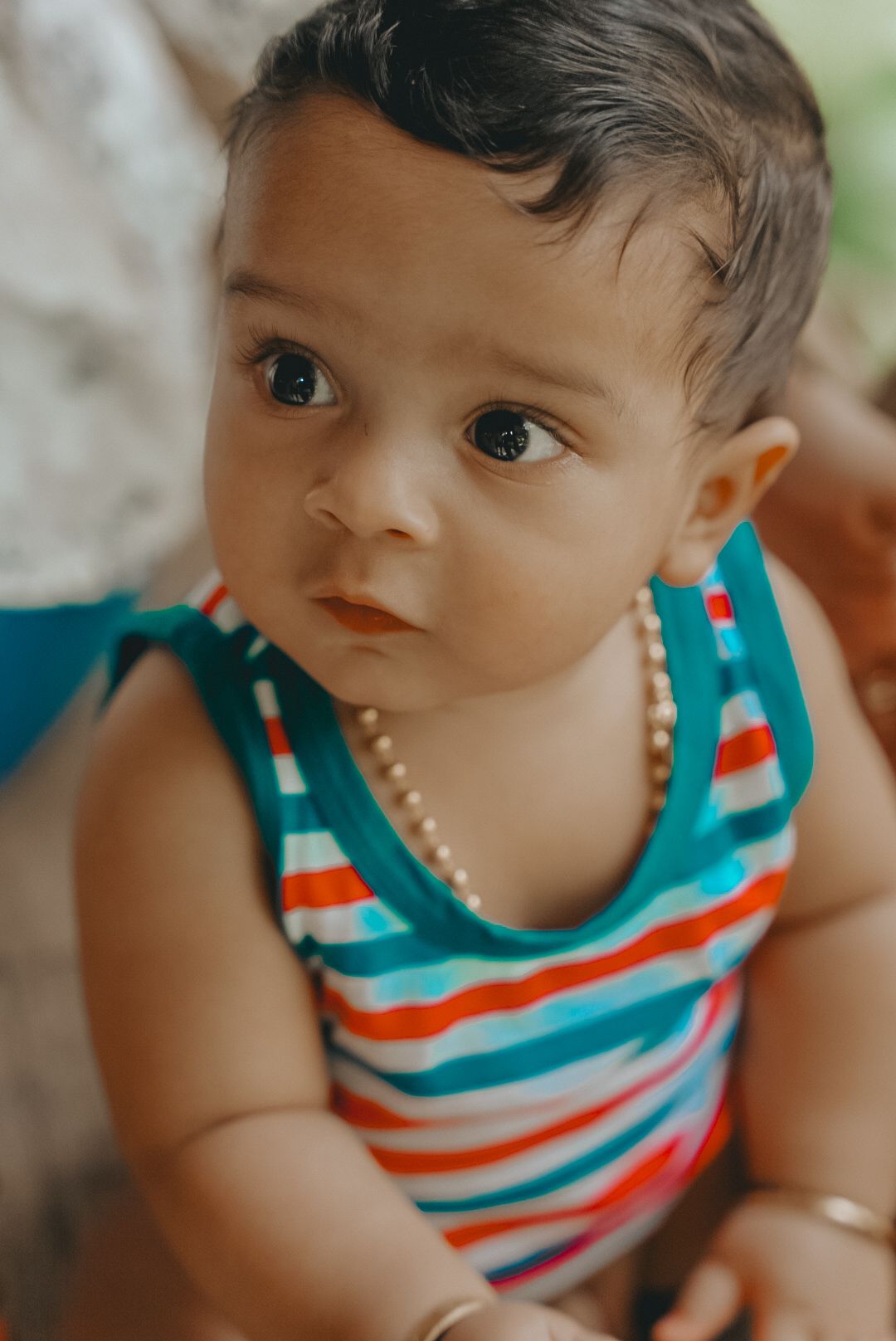 Close-up portraits of an infant wearing a colorful striped outfit with turquoise and orange details.