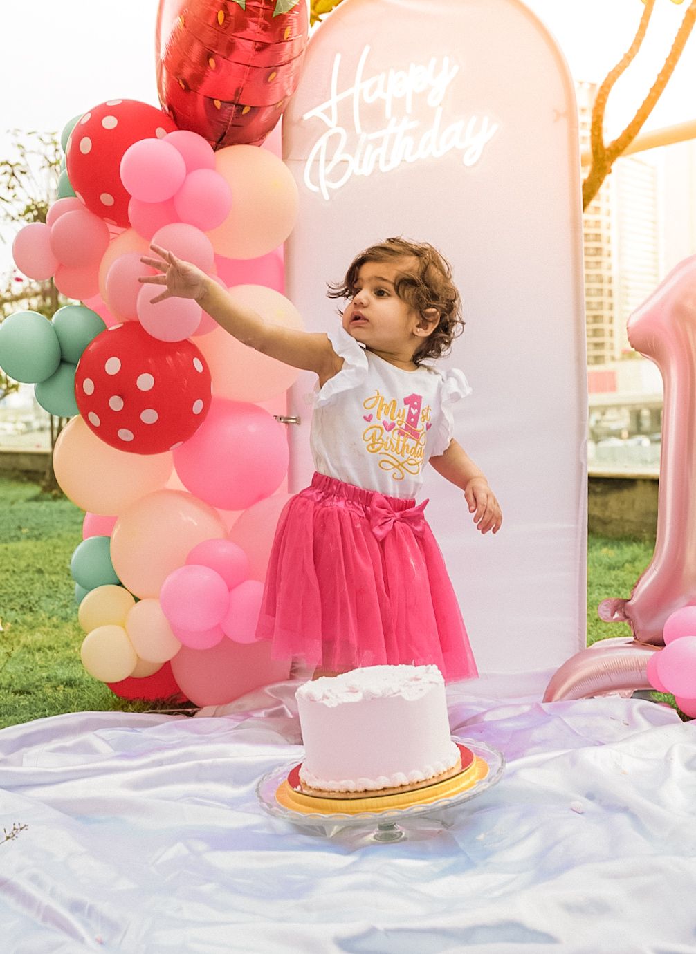 Birthday party setup with pink balloon arch and decorations against white backdrop.