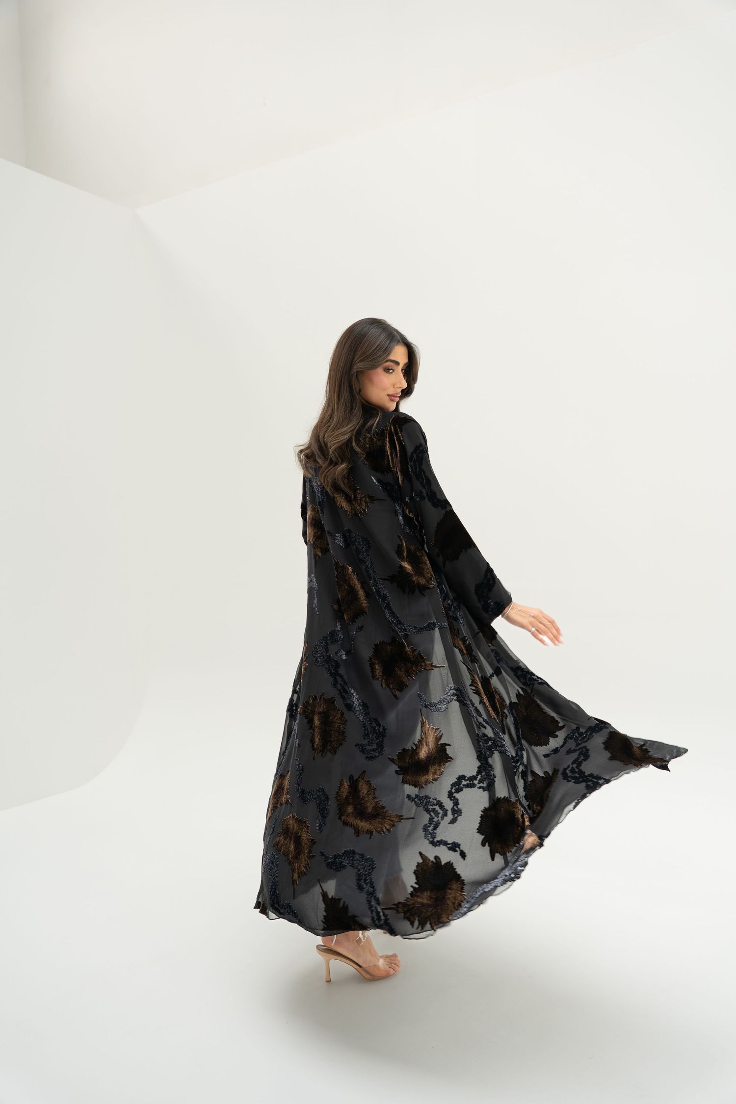 A figure in a flowing black lace dress performs an expressive dance movement against a white backdrop.