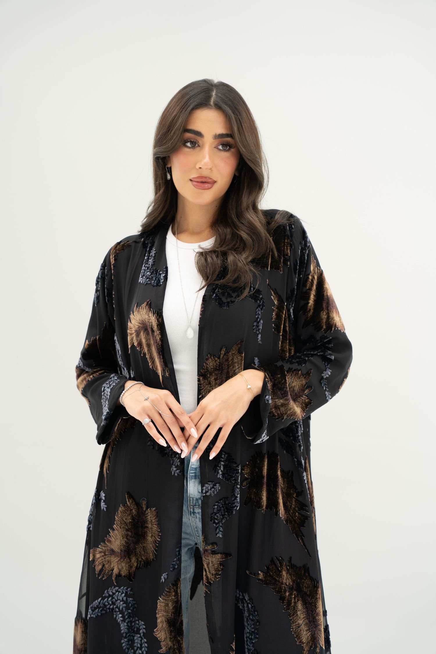 Model wearing a black and brown tie-dye pattern long cardigan with white top and jeans against white background.