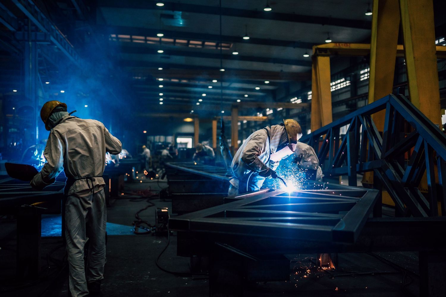Blue-lit industrial welding operations in a manufacturing facility at night.