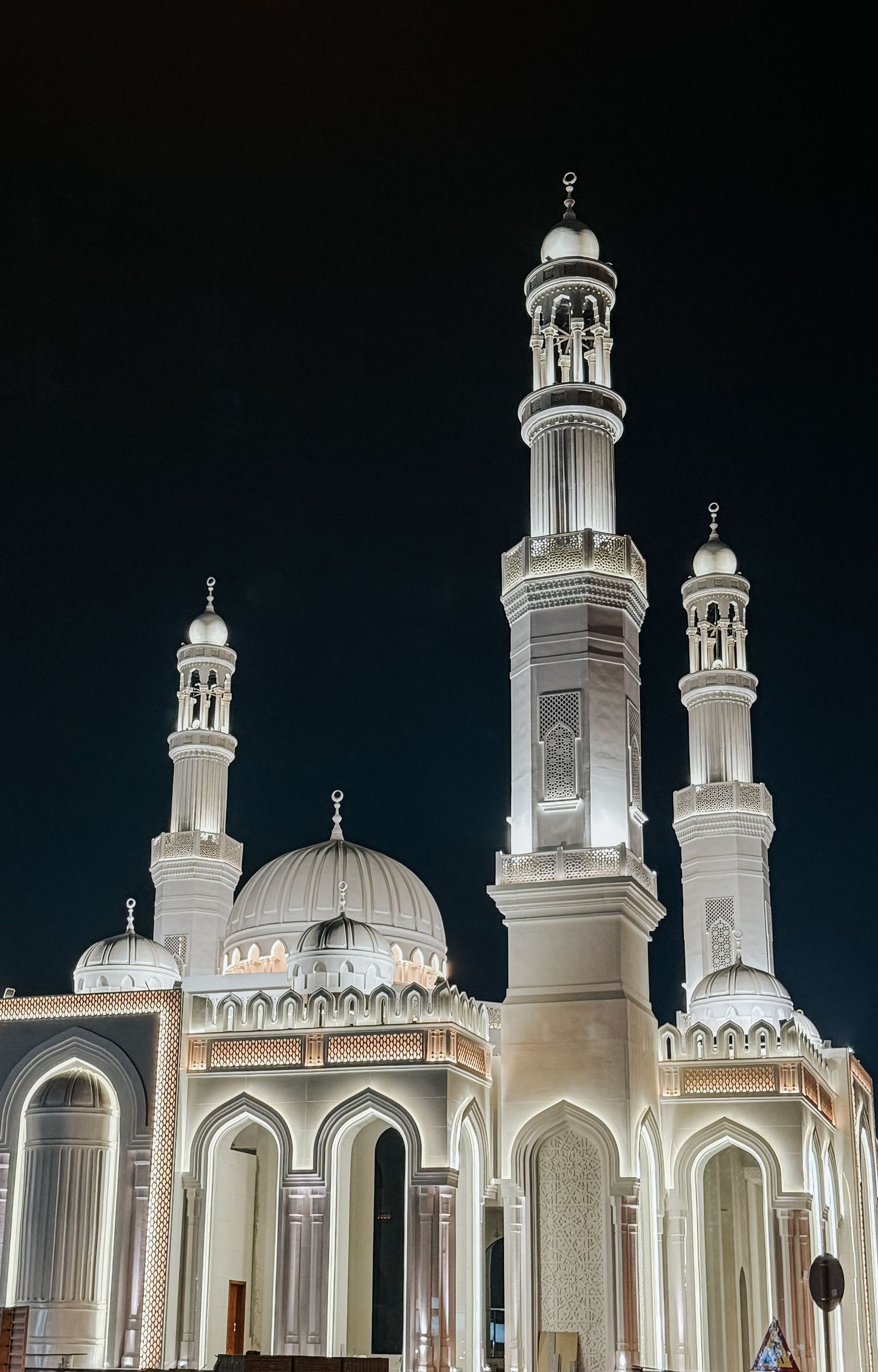 Illuminated white mosque with multiple minarets and domes against a dark night sky.