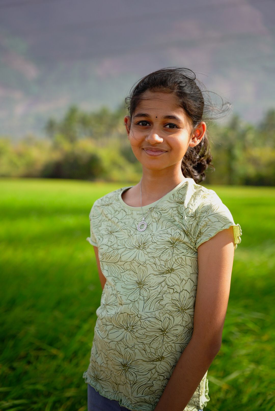 Portrait series in a green field wearing a white floral lace top against a mountain backdrop.