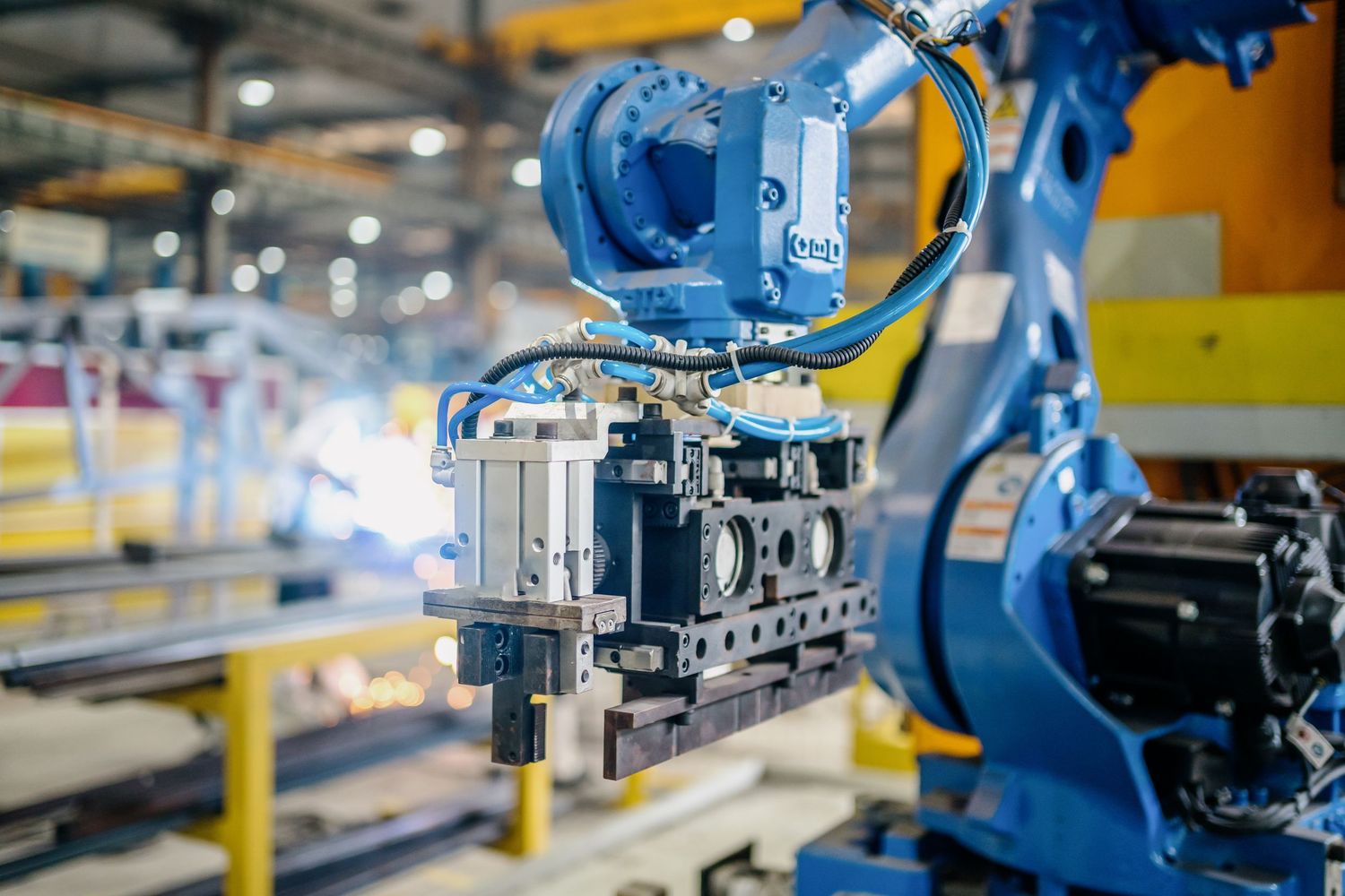 Industrial robotic arms operate in automated manufacturing facility with blue and yellow elements.