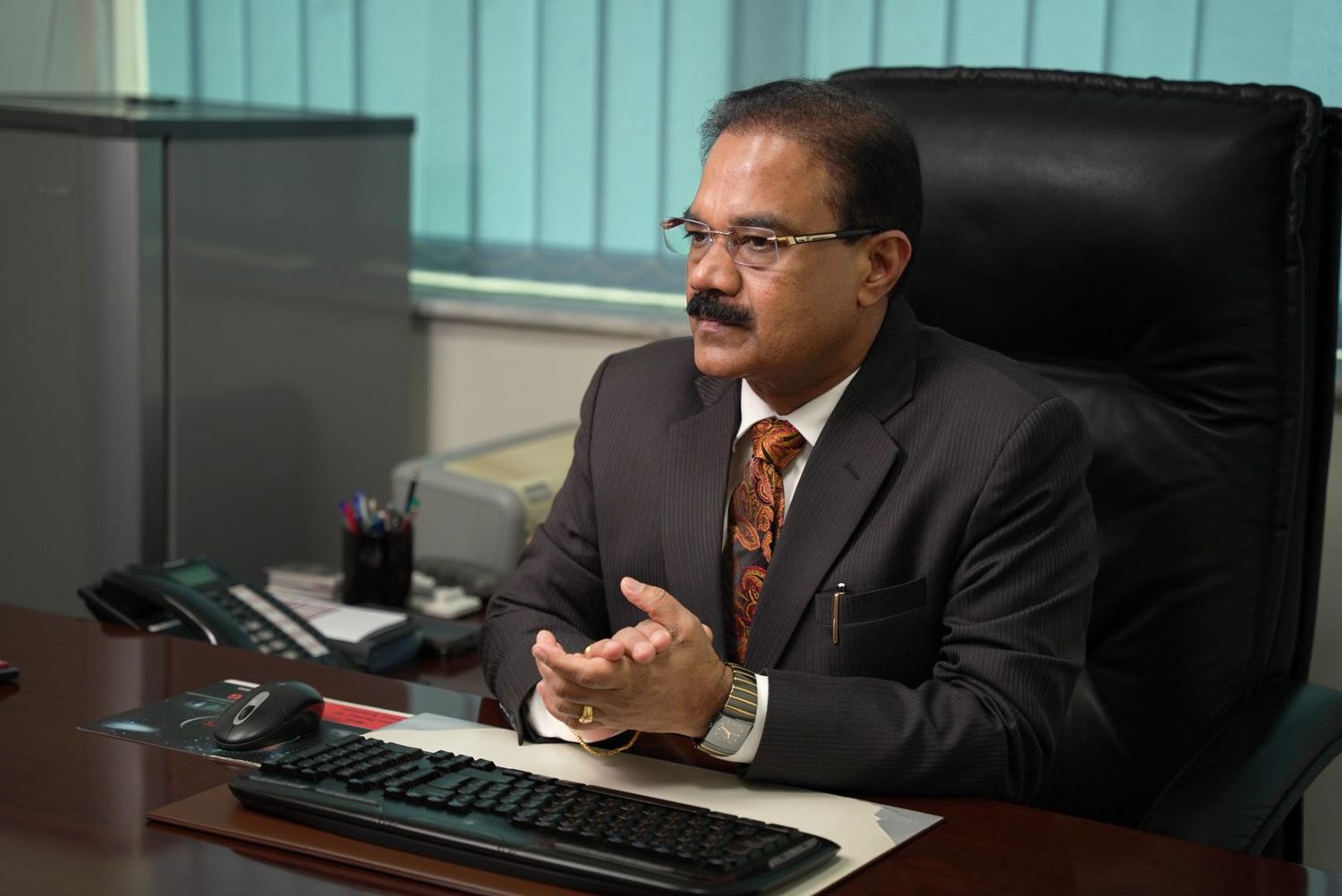 Professional wearing a suit sits at an office desk while looking at computer monitors in a corporate setting.