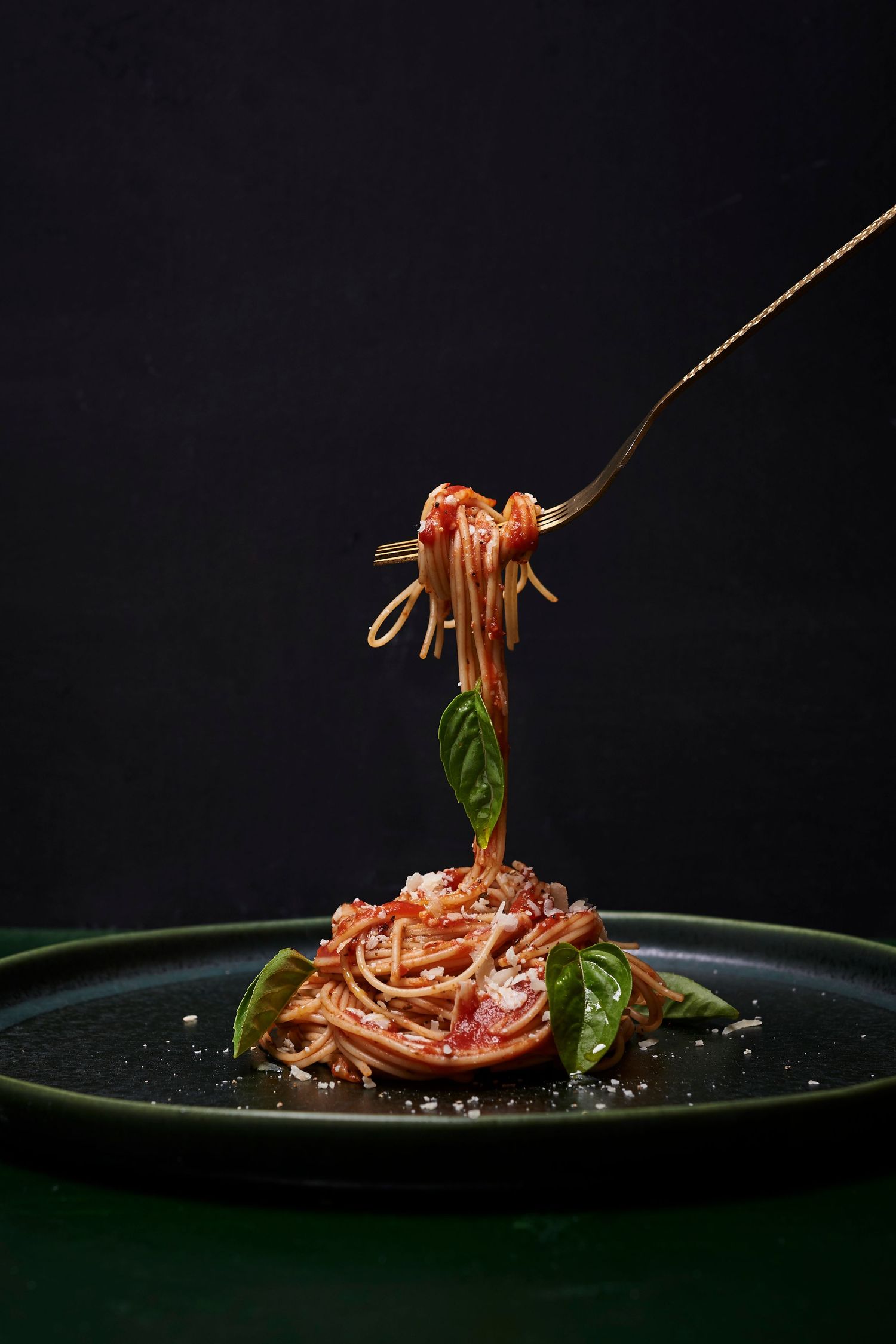 Artistic food photography of pasta being lifted with fork against dark background.