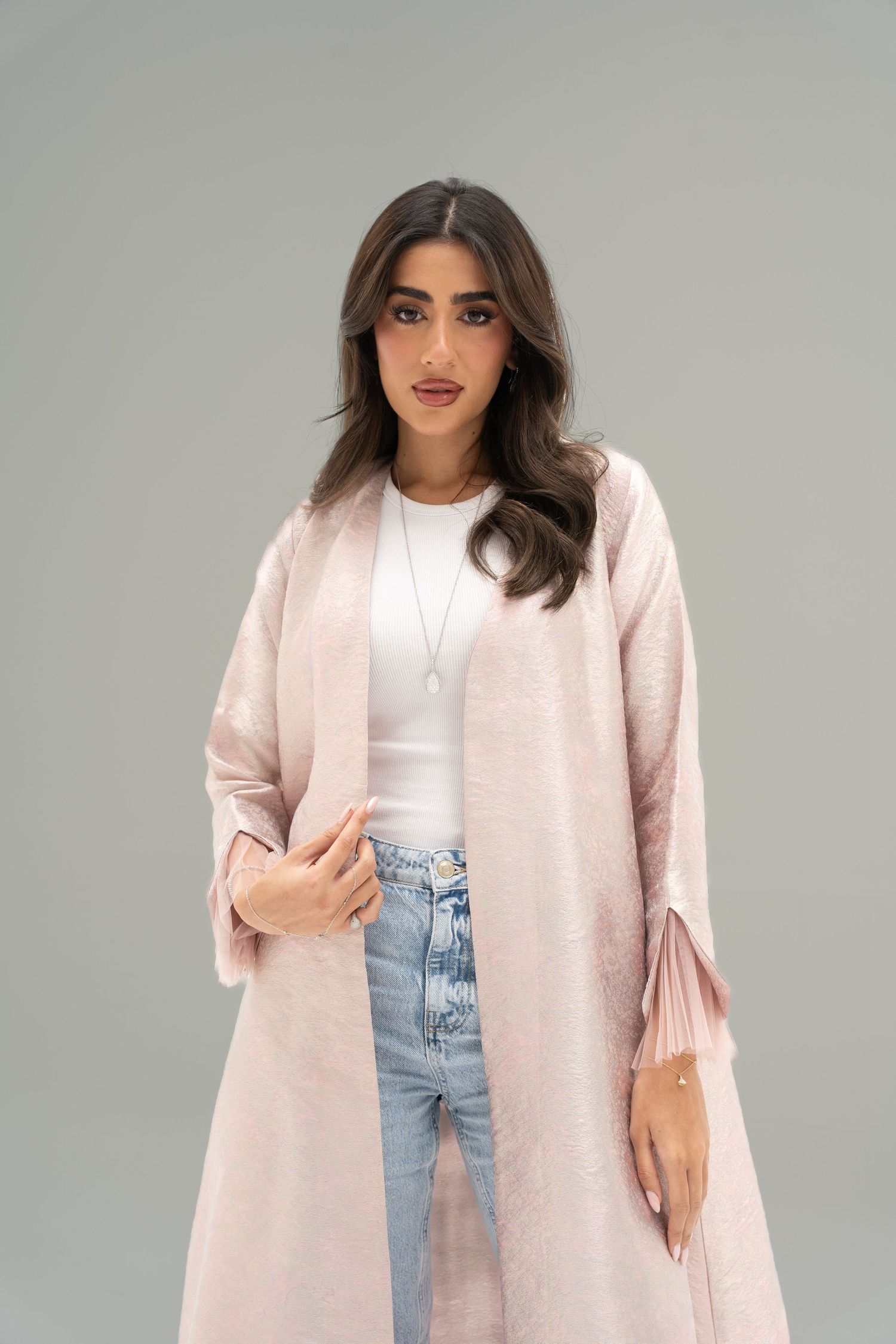 Model wearing a light pink longline cardigan over white top and light wash jeans against grey background.