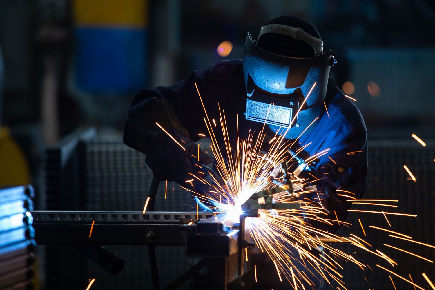 Welding sparks flying in a dark industrial workshop during metal fabrication.