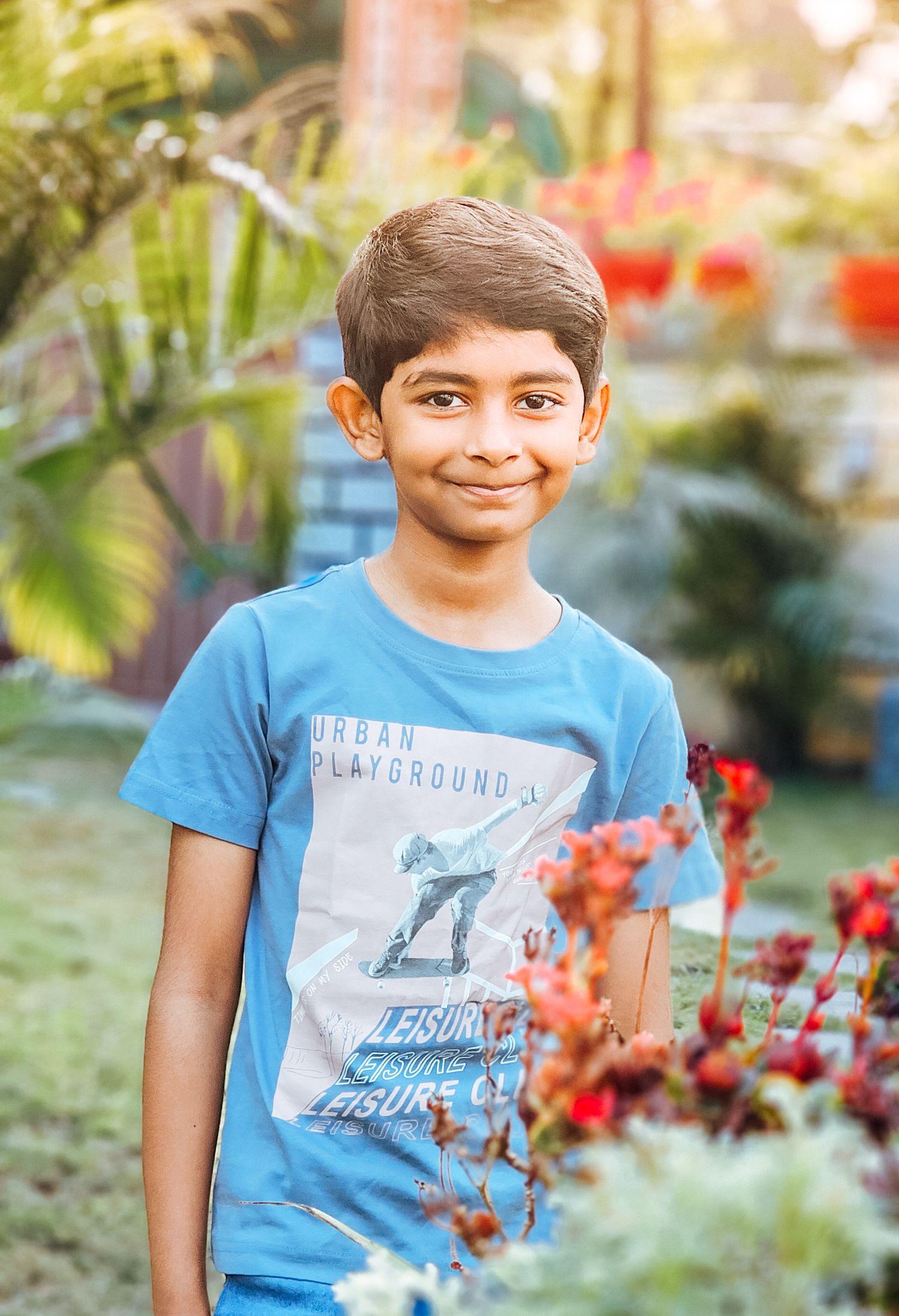 A series of outdoor portraits showing a child in a blue graphic t-shirt against a garden background with red flowers.