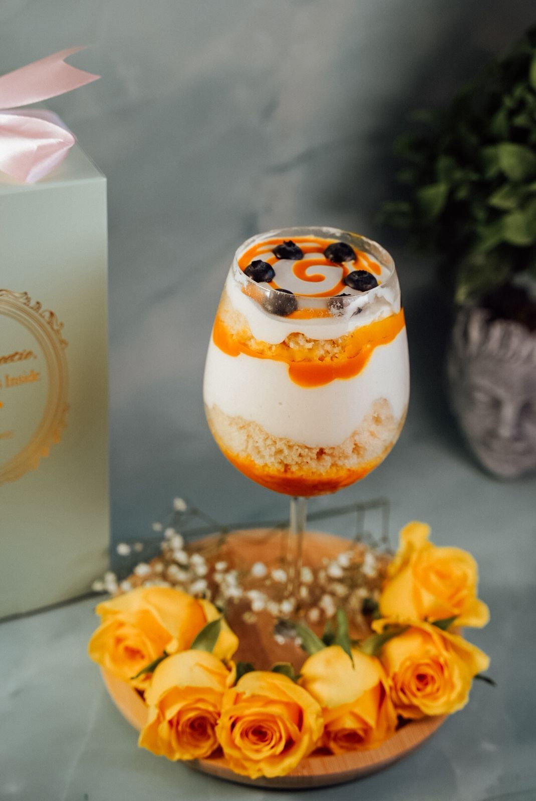 Elegant cocktail garnished with orange peel and berries, surrounded by yellow roses.
