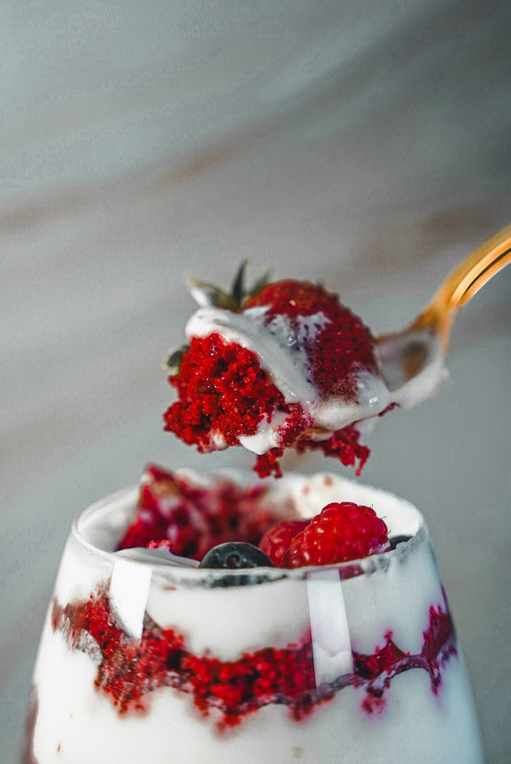 Creamy dessert topped with fresh red berries and whipped cream in a glass.
