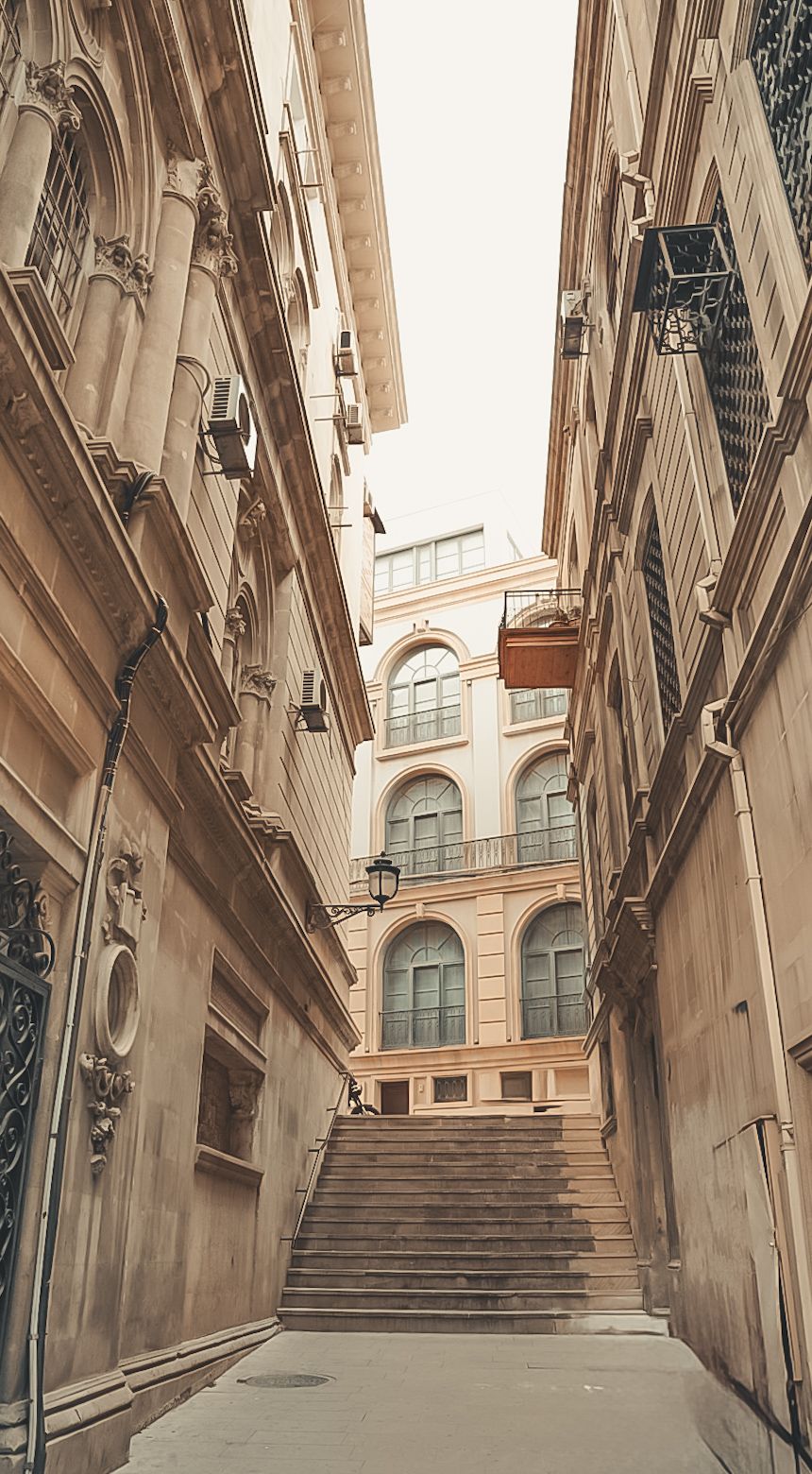 Architectural view of a historic corridor with arched windows and stone staircase.