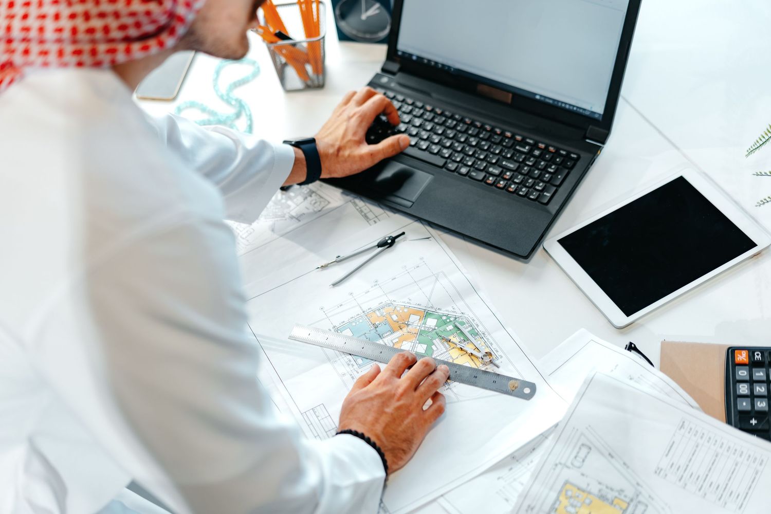 Medical professional reviews documents at desk with laptop and digital devices.