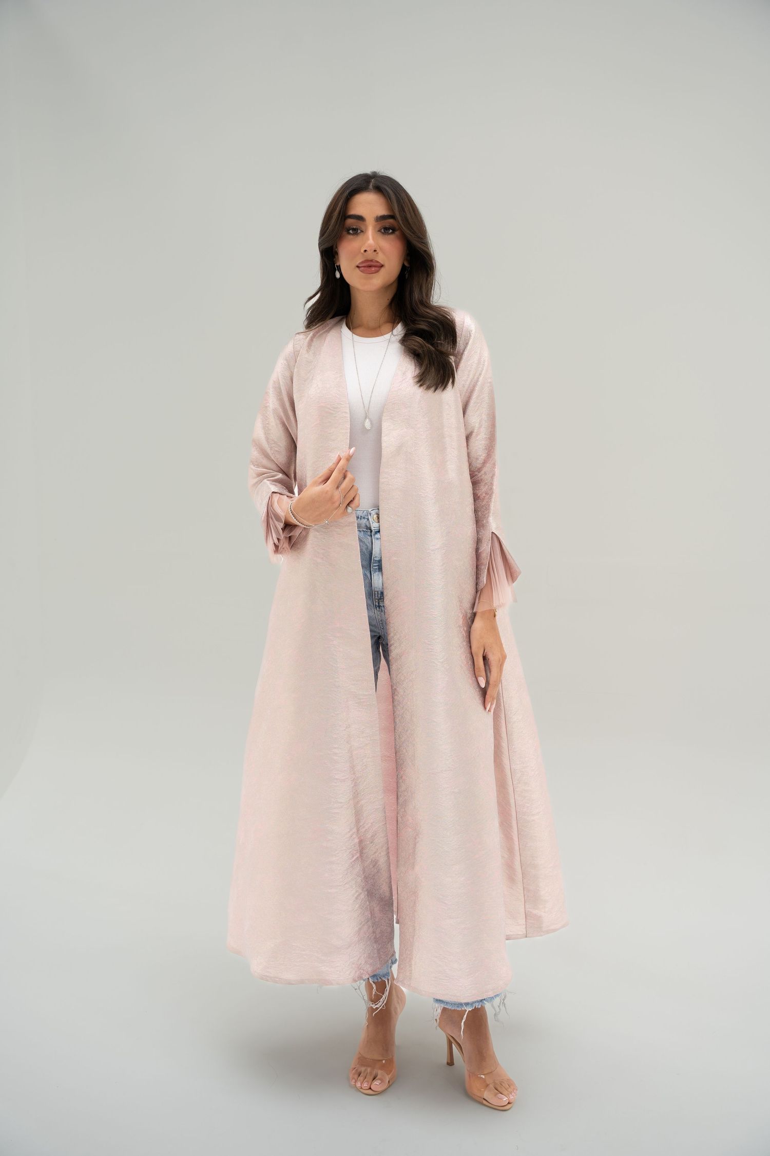 A pink linen duster coat styled with light denim and neutral sandals in a minimalist studio setting.