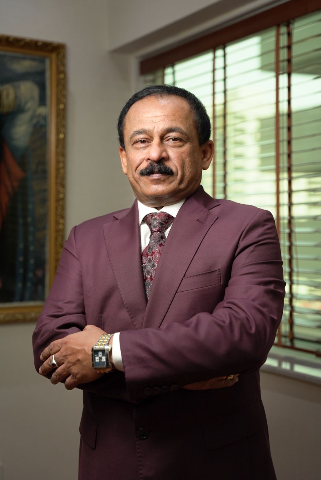 Professional portrait in burgundy suit against window light background.