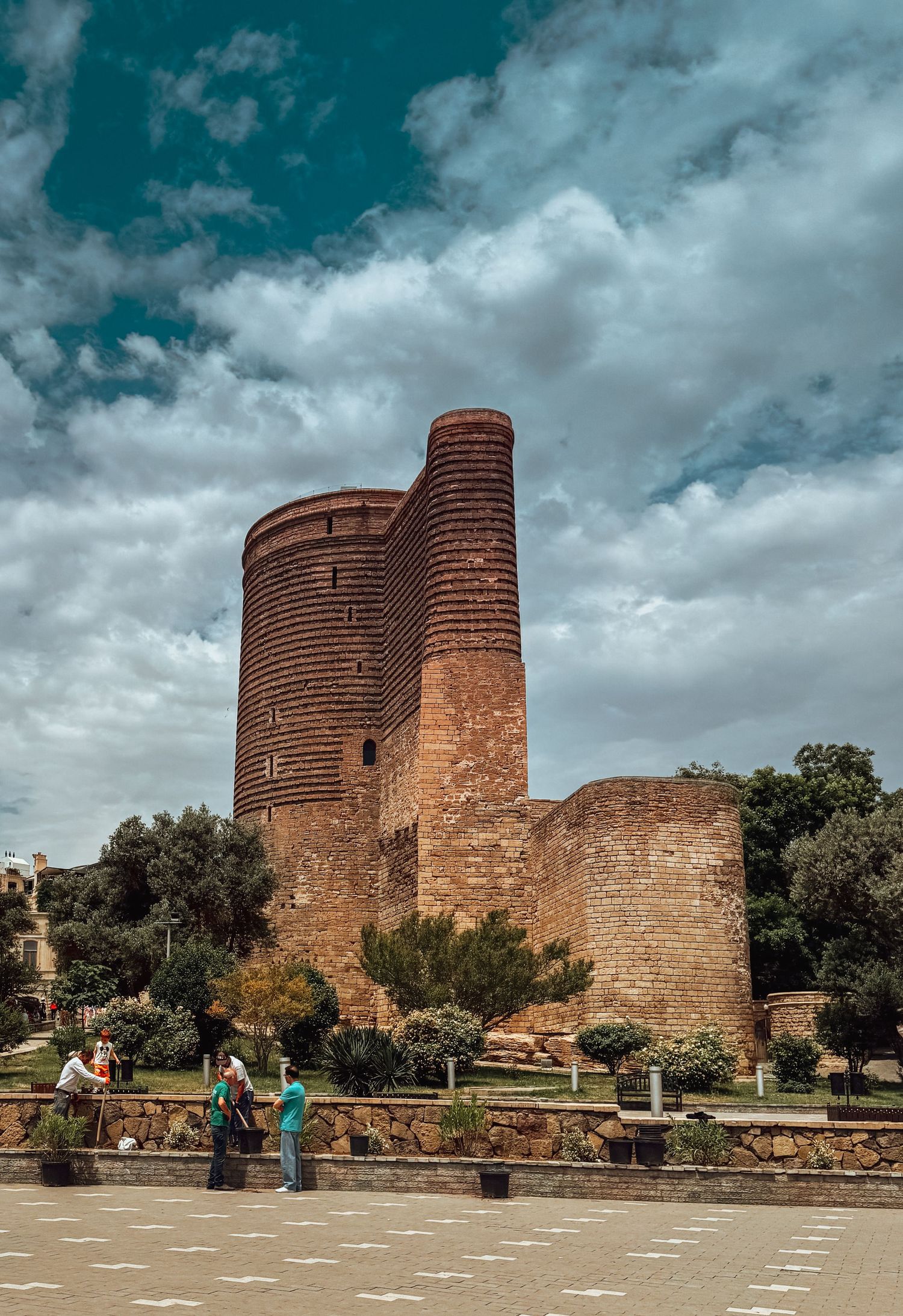 Ancient stone towers of the Maiden Tower in Baku against a dramatic cloudy sky.