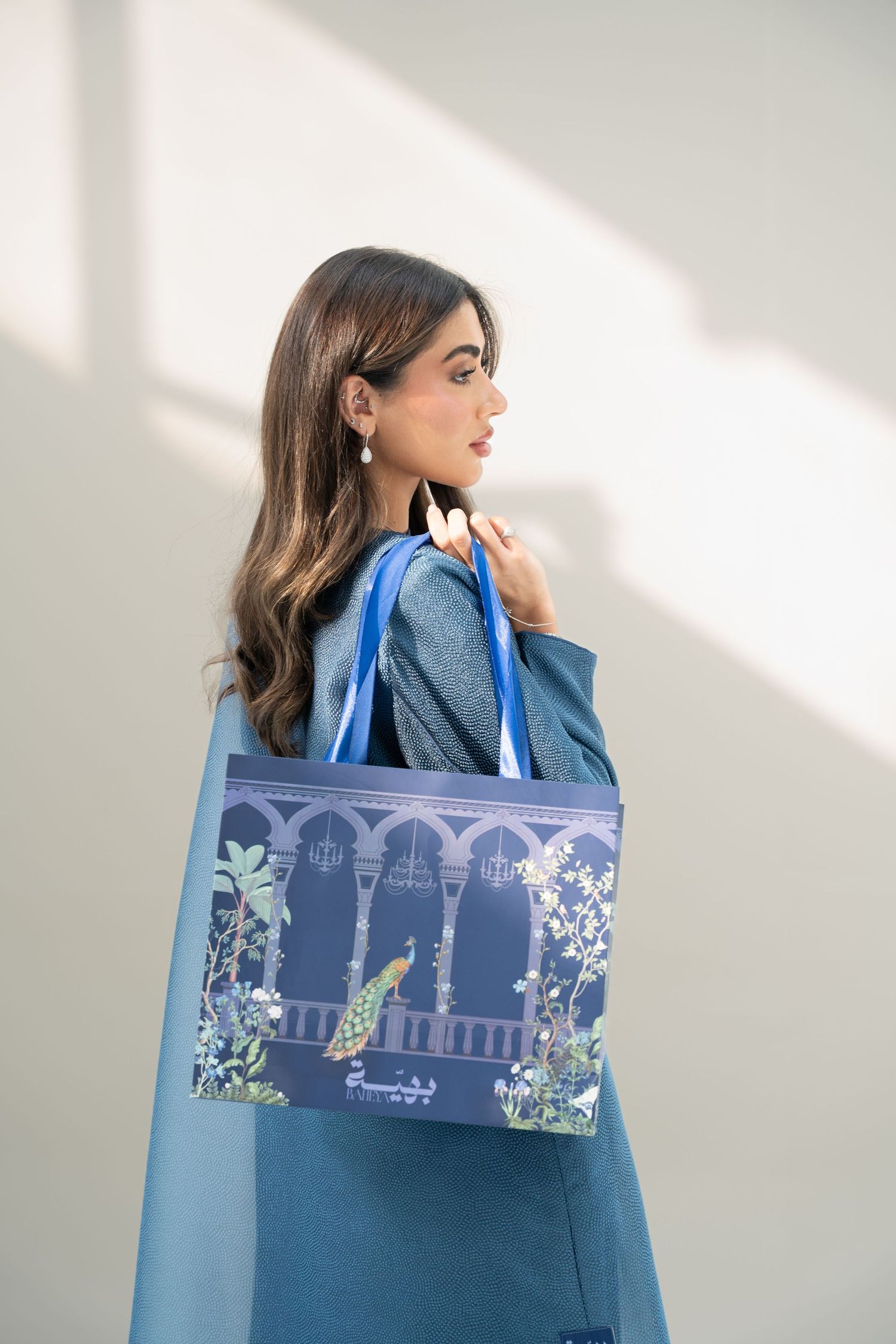 A person in blue attire poses with a decorative blue tote bag featuring architectural designs and floral patterns.