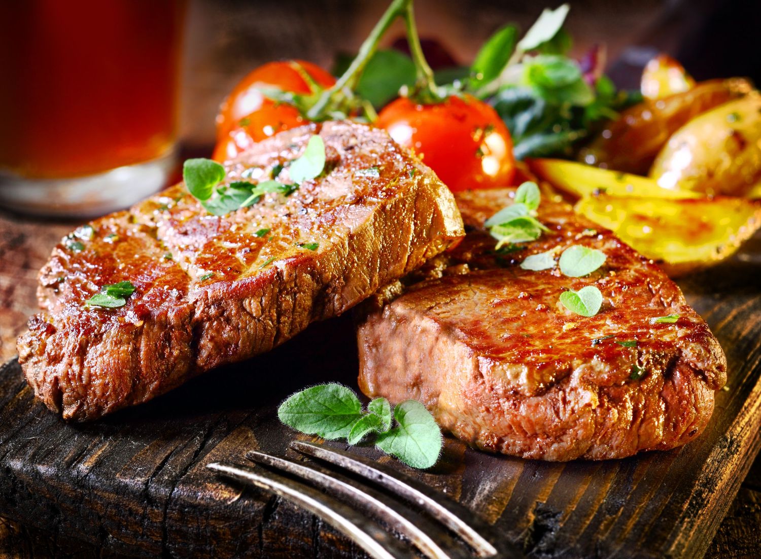 Grilled steaks with herbs and seasonings on a dark cooking surface.