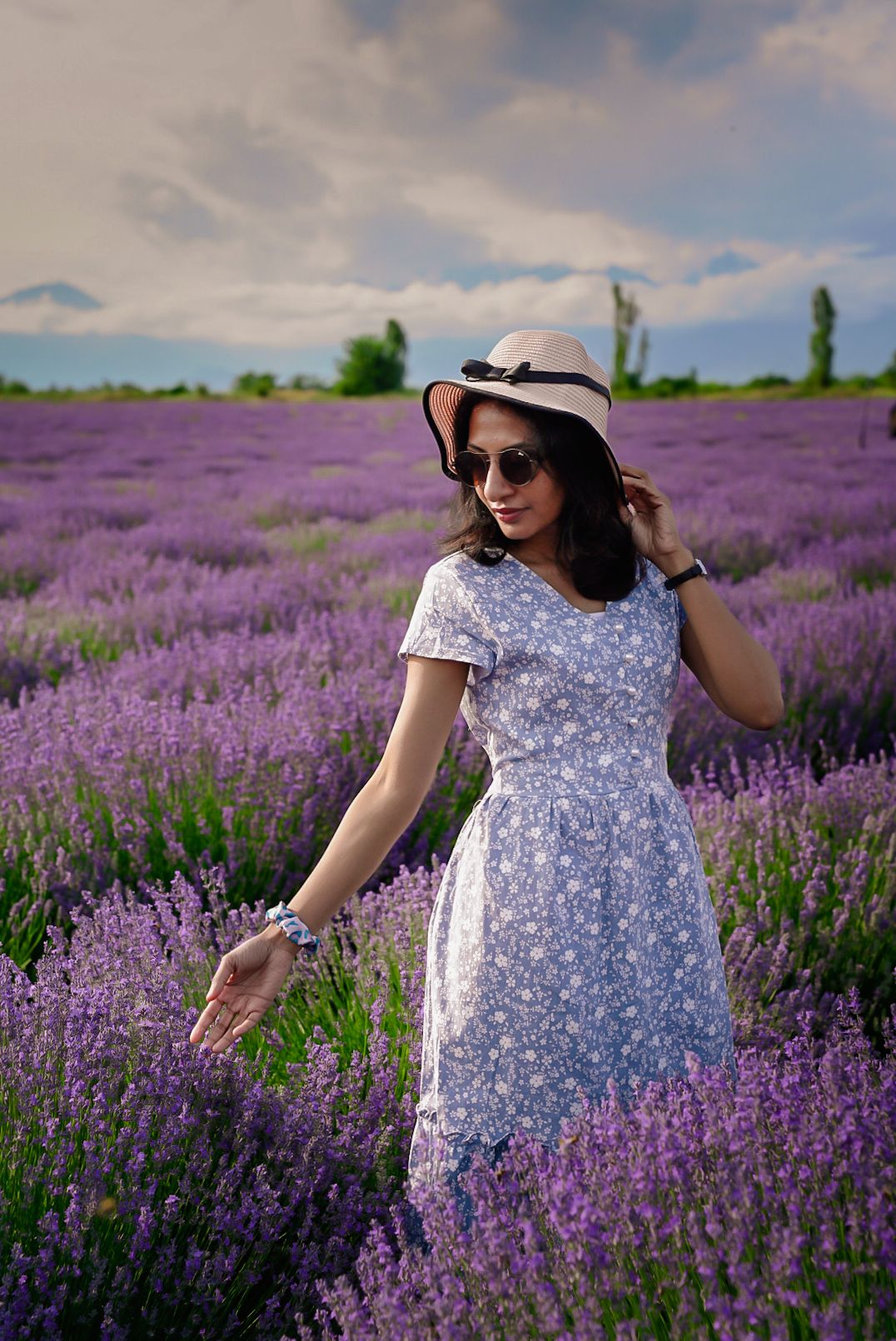 Woman in floral dress walking through blooming purple lavender field on sunny day.