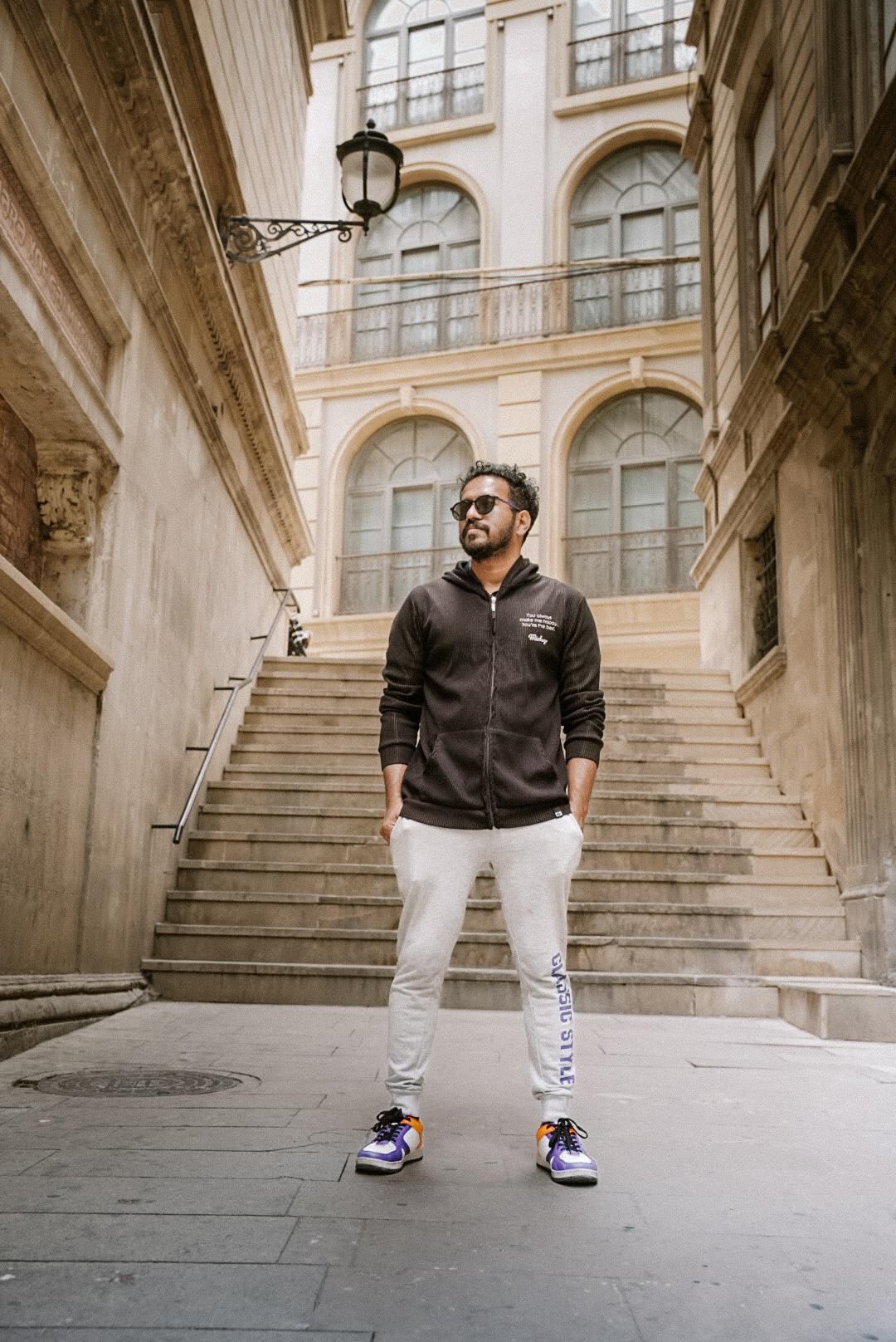Man in casual wear posing against grand architectural staircase in historic building.